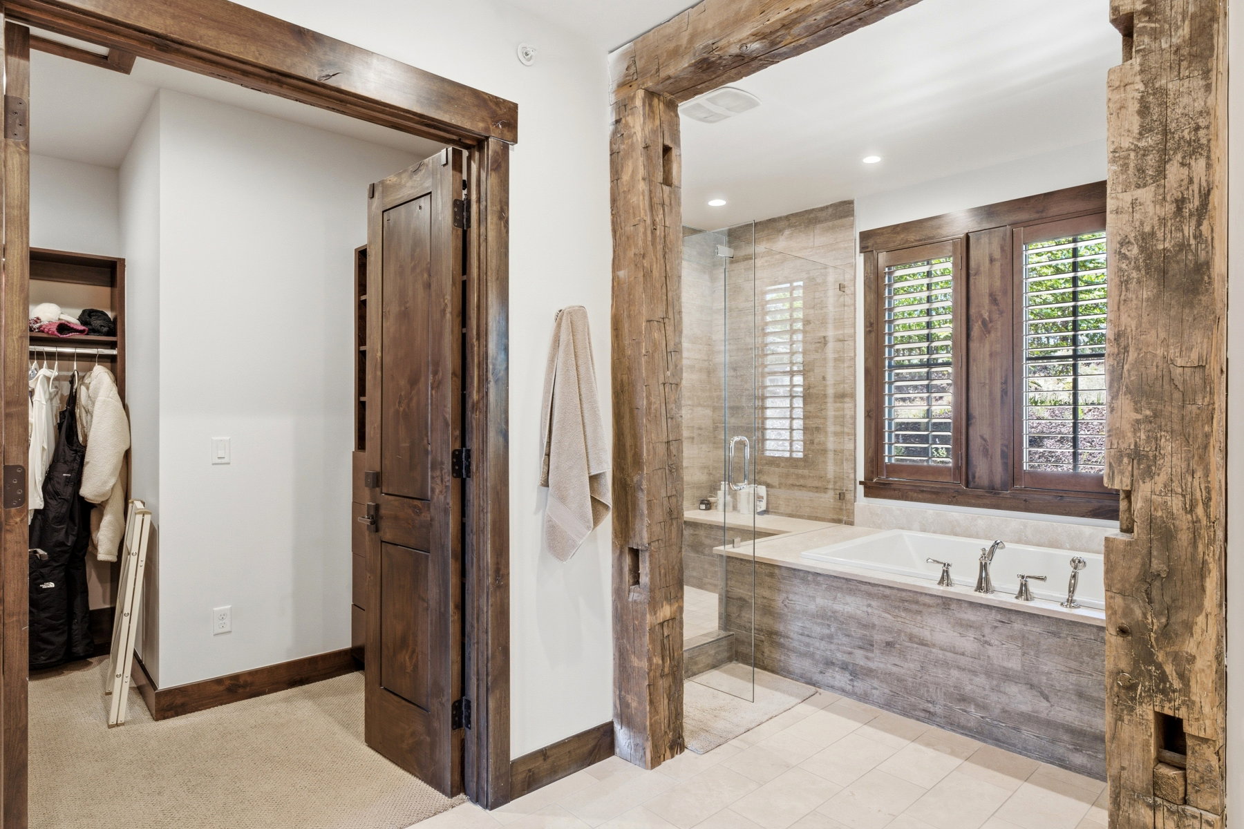 Bathroom featuring a built-in soaking tub with a tiled surround, a glass-enclosed shower, and wood-framed windows with louvered shutters
