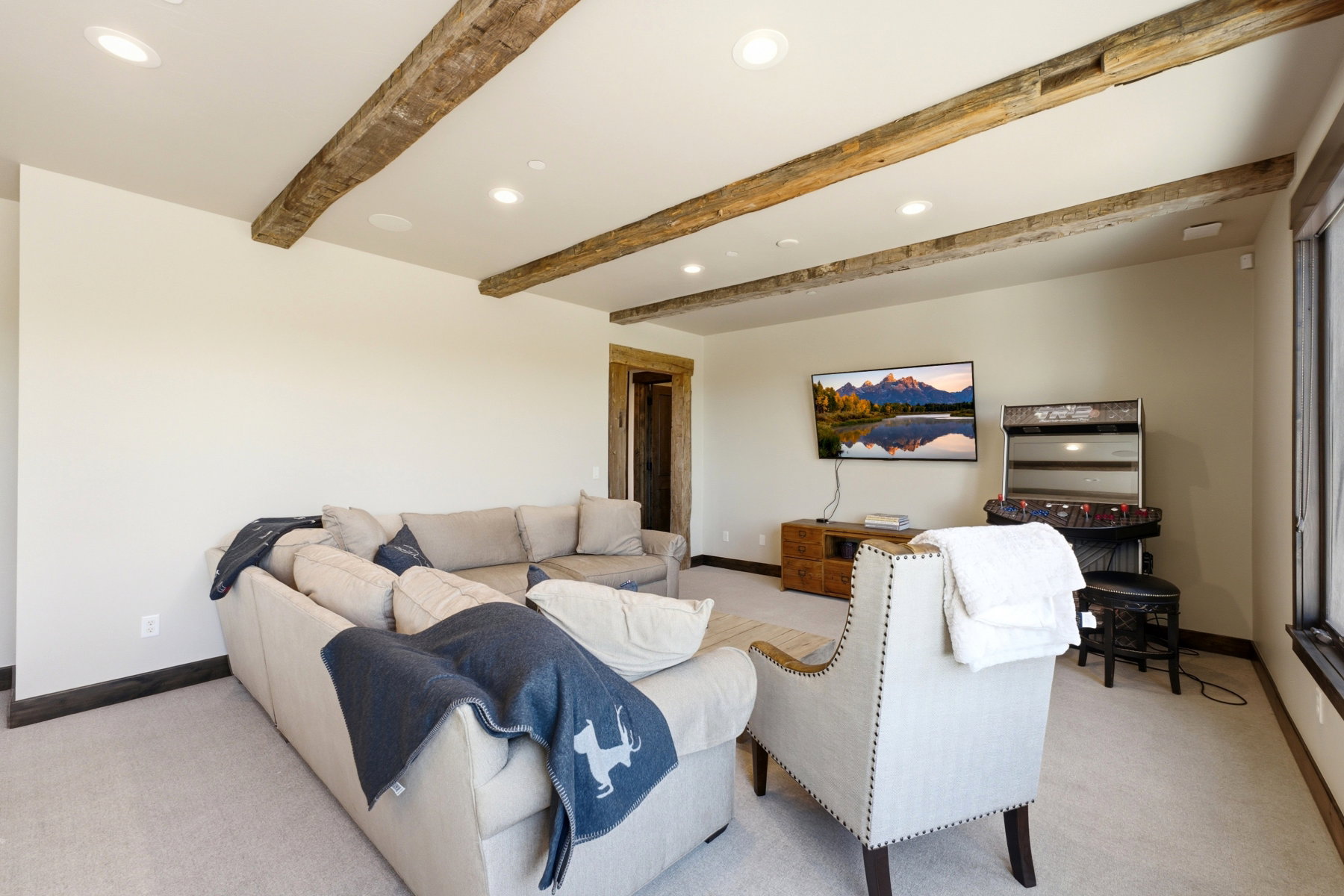 Living area featuring exposed wood beams, recessed lighting, carpet flooring, a wood-finish entertainment console, and a large window with dark trim