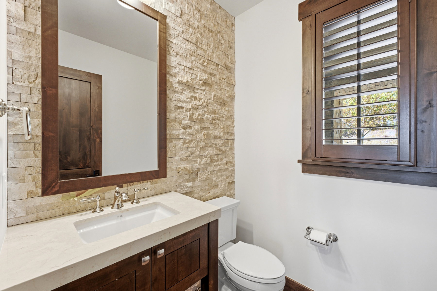 Bathroom featuring a stone accent wall, dark wood vanity with a light-toned countertop, and an undermount sink with a polished chrome faucet