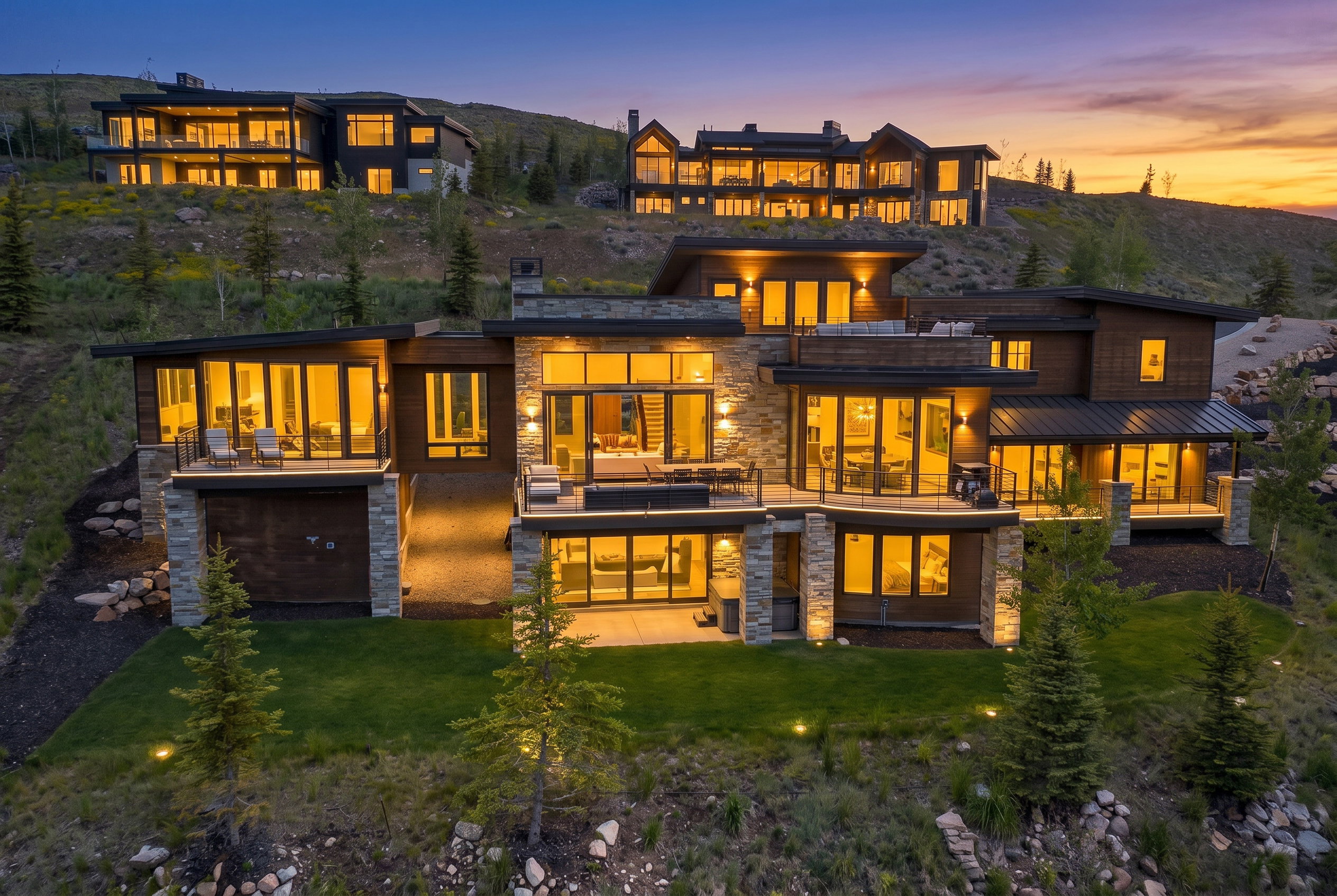Modern architectural residence featuring multiple levels of outdoor living spaces, expansive window walls, stone accents, and a tiered landscaped yard