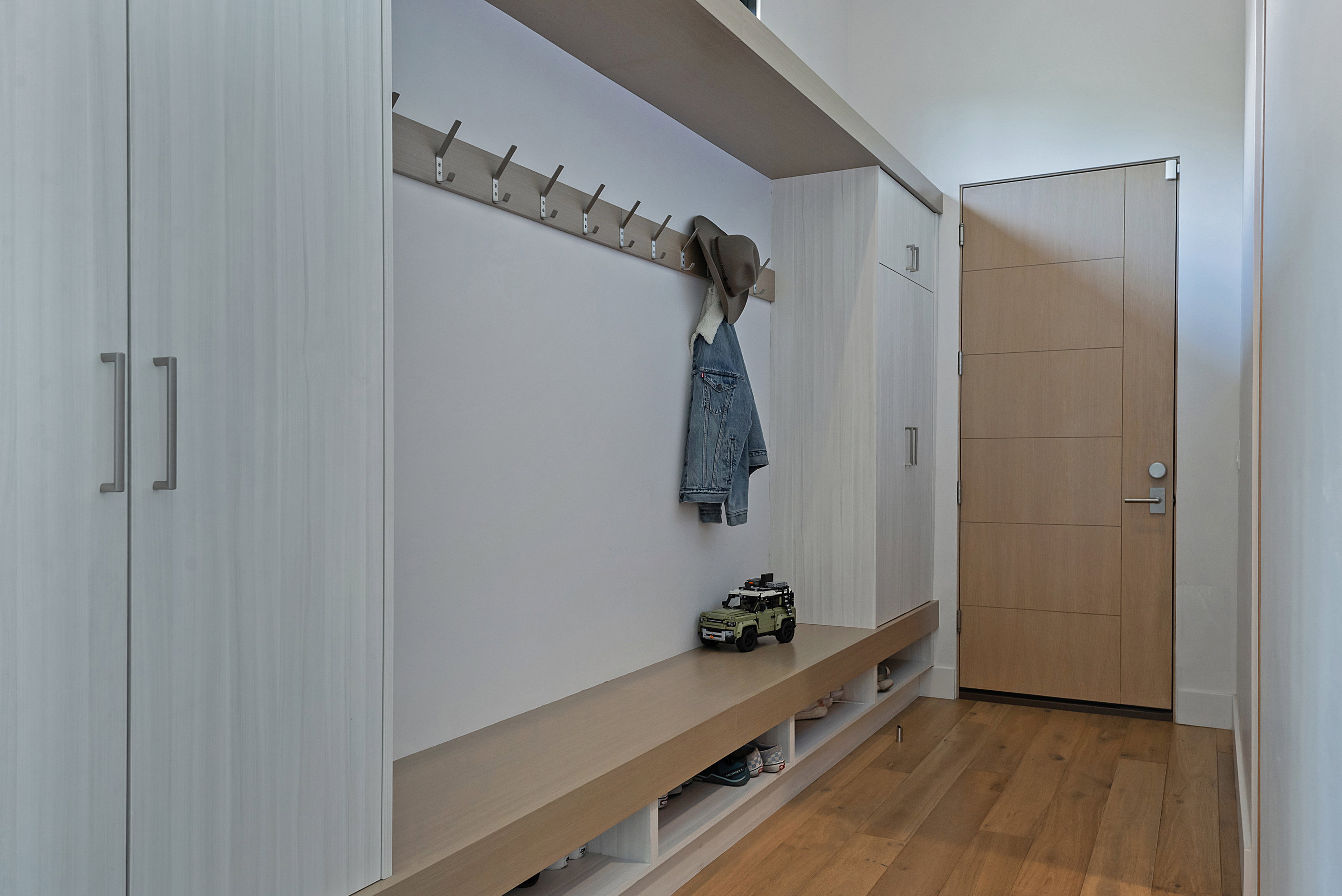 Entryway featuring built-in cabinetry, integrated bench seating, wall-mounted coat hooks, and wood-finish flooring