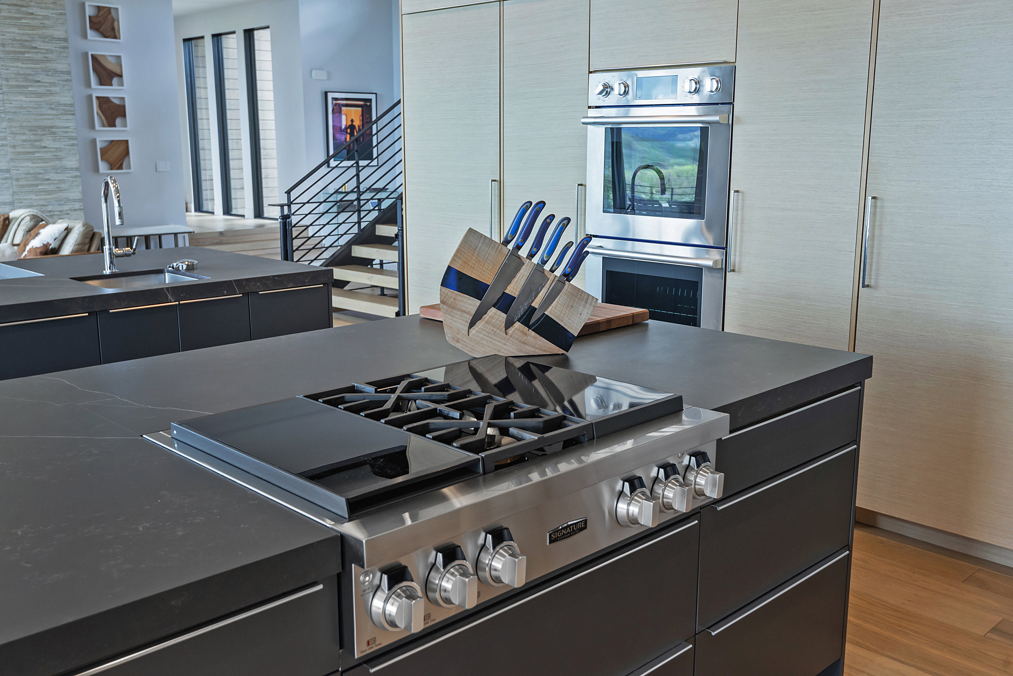 Gourmet kitchen featuring a built-in stainless steel range, double wall ovens, dark stone countertops, custom cabinetry, and wood-finish flooring