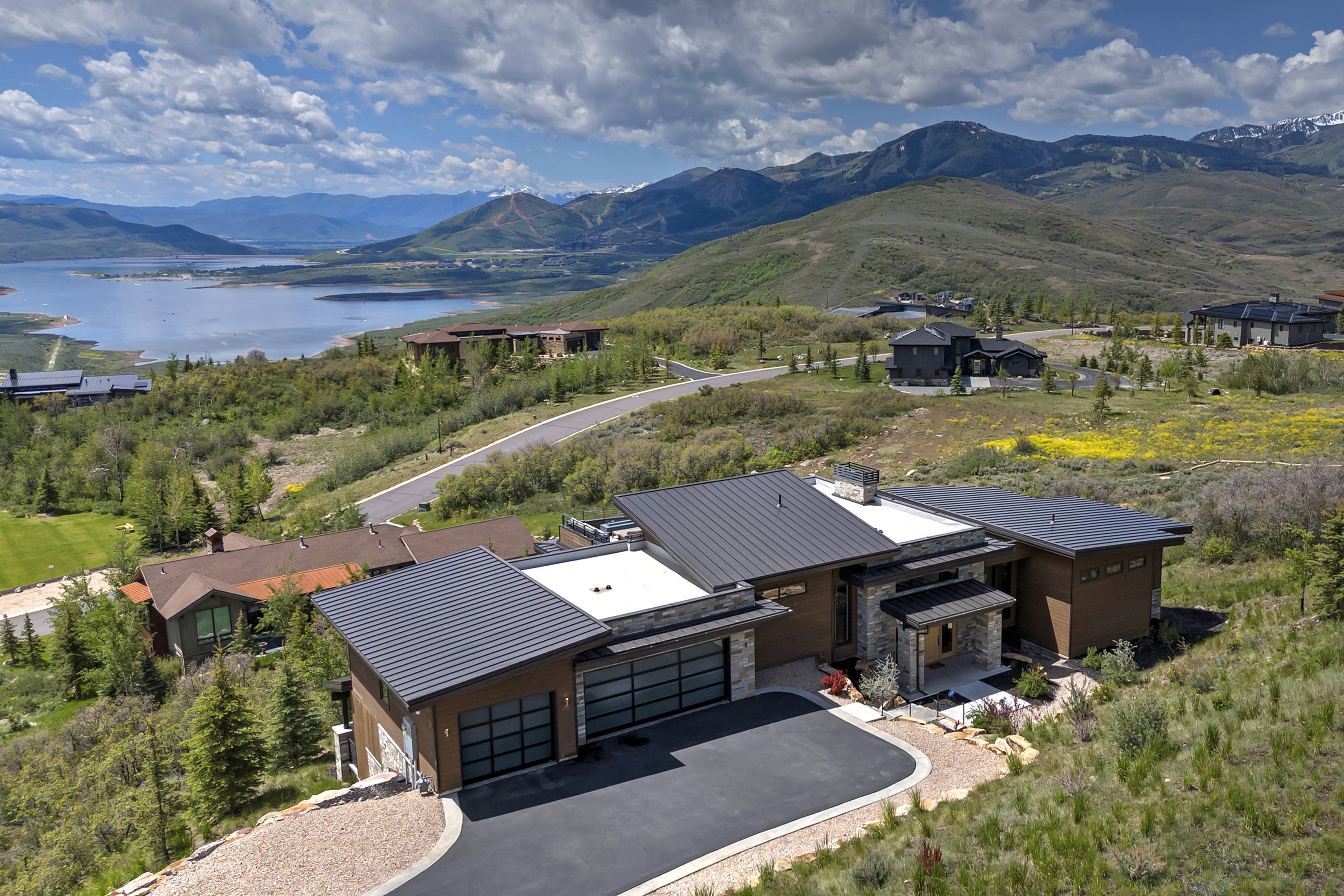 Contemporary mountain home featuring a dark metal roof, stone accents, two-car garage with frosted glass doors, a paved driveway, and mountain scenery