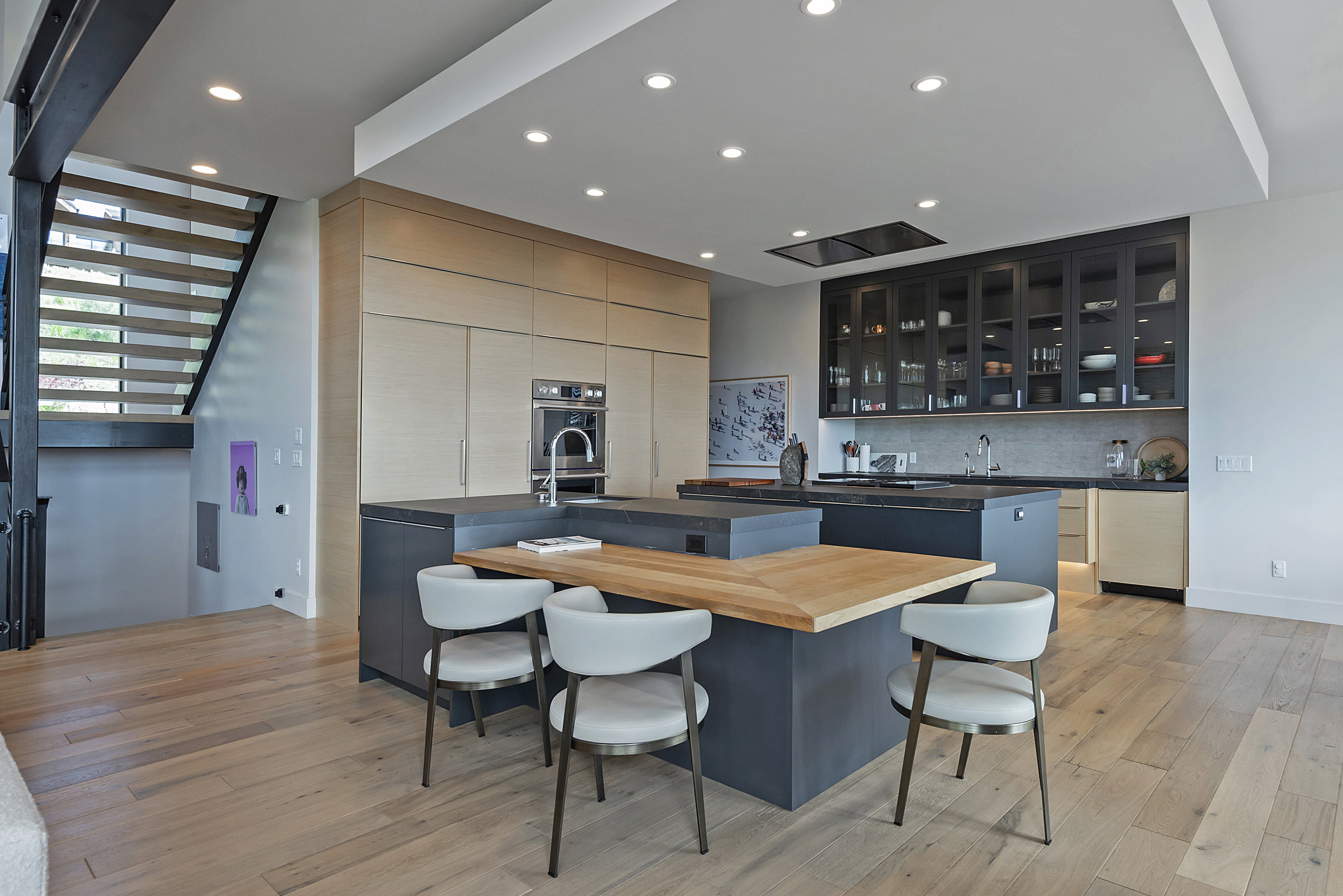 Gourmet kitchen featuring a large central island with integrated seating, light wood-finish flooring, recessed lighting, and a built-in oven
