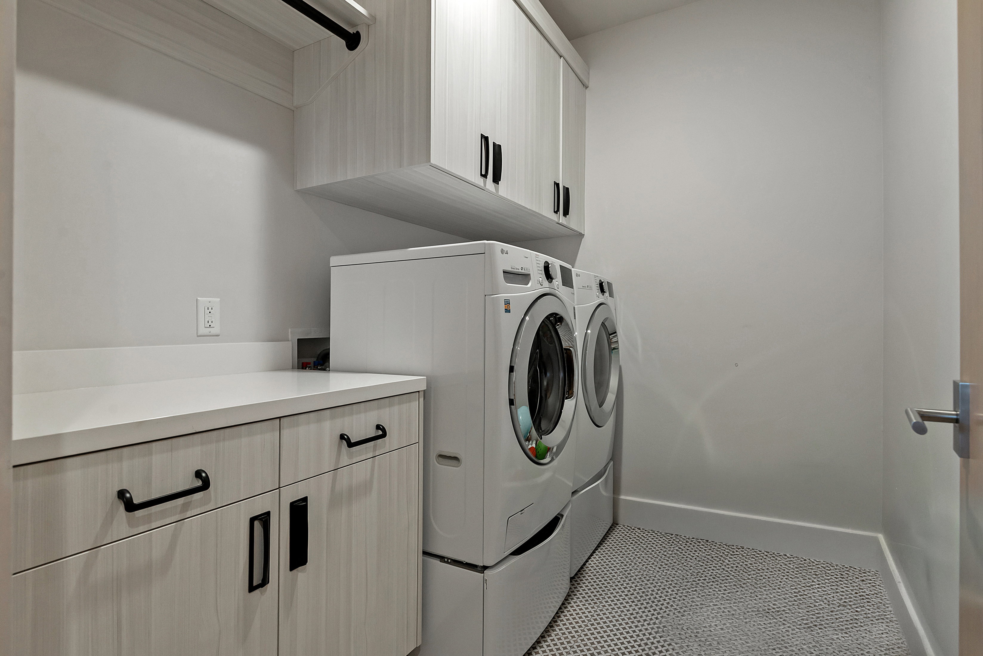 Laundry area featuring light wood-finish cabinetry, white countertops, built-in upper storage, a black hanging rod, and hex-patterned floor tiling