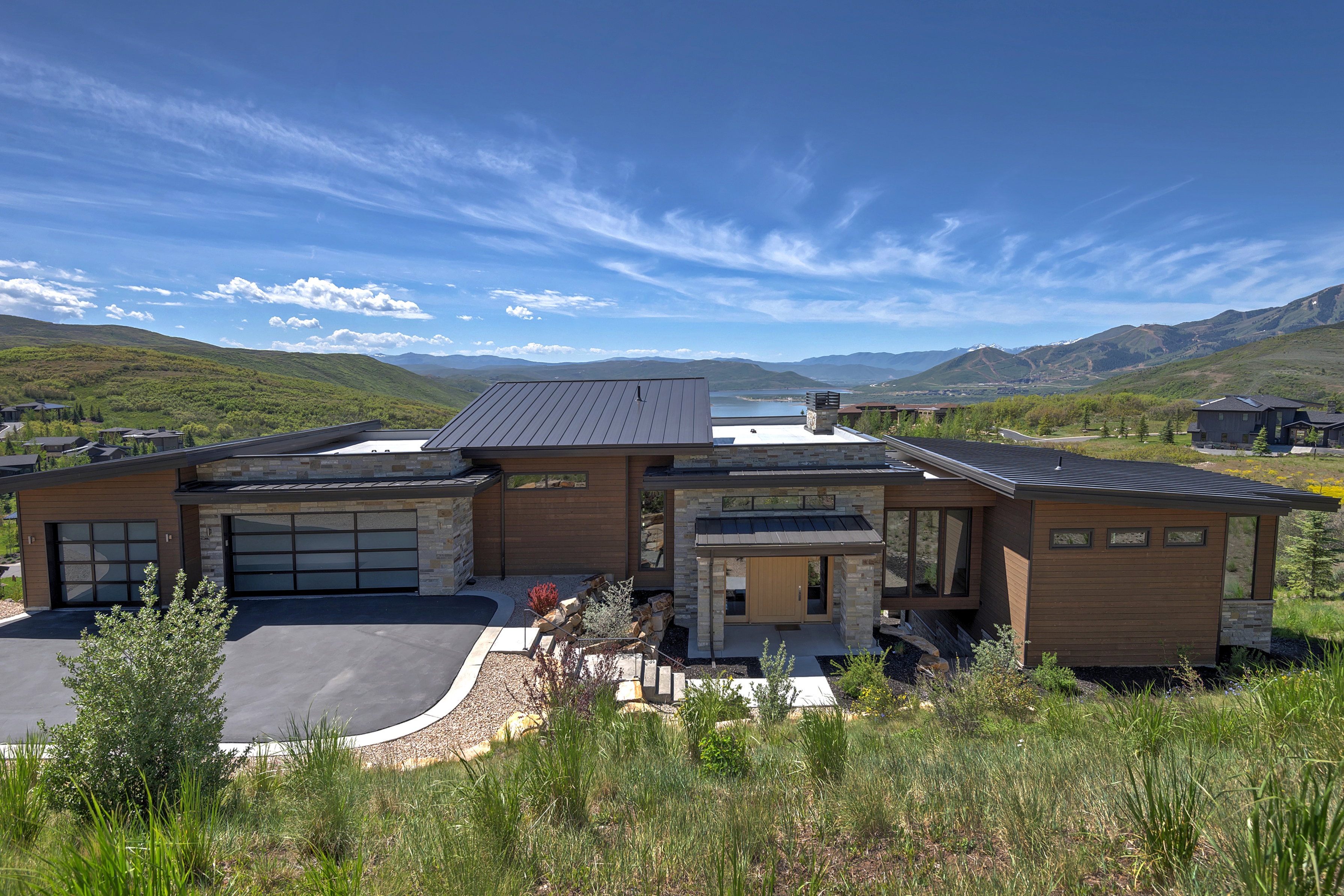 Modern architectural exterior featuring wood-finish siding, stone accents, and a metal roof