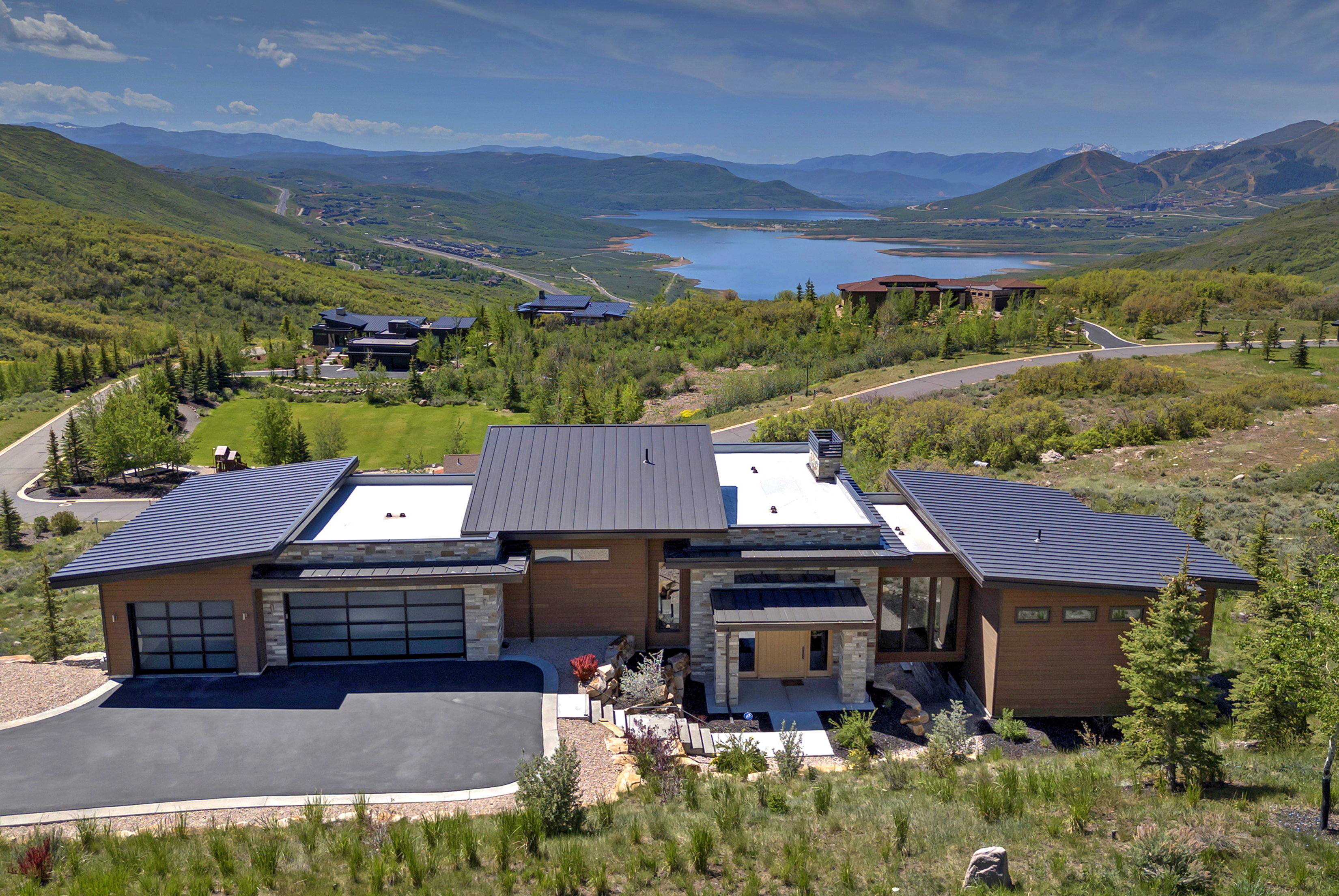 Modern architectural residence featuring a metal roof, stone facade accents, and an expansive paved driveway
