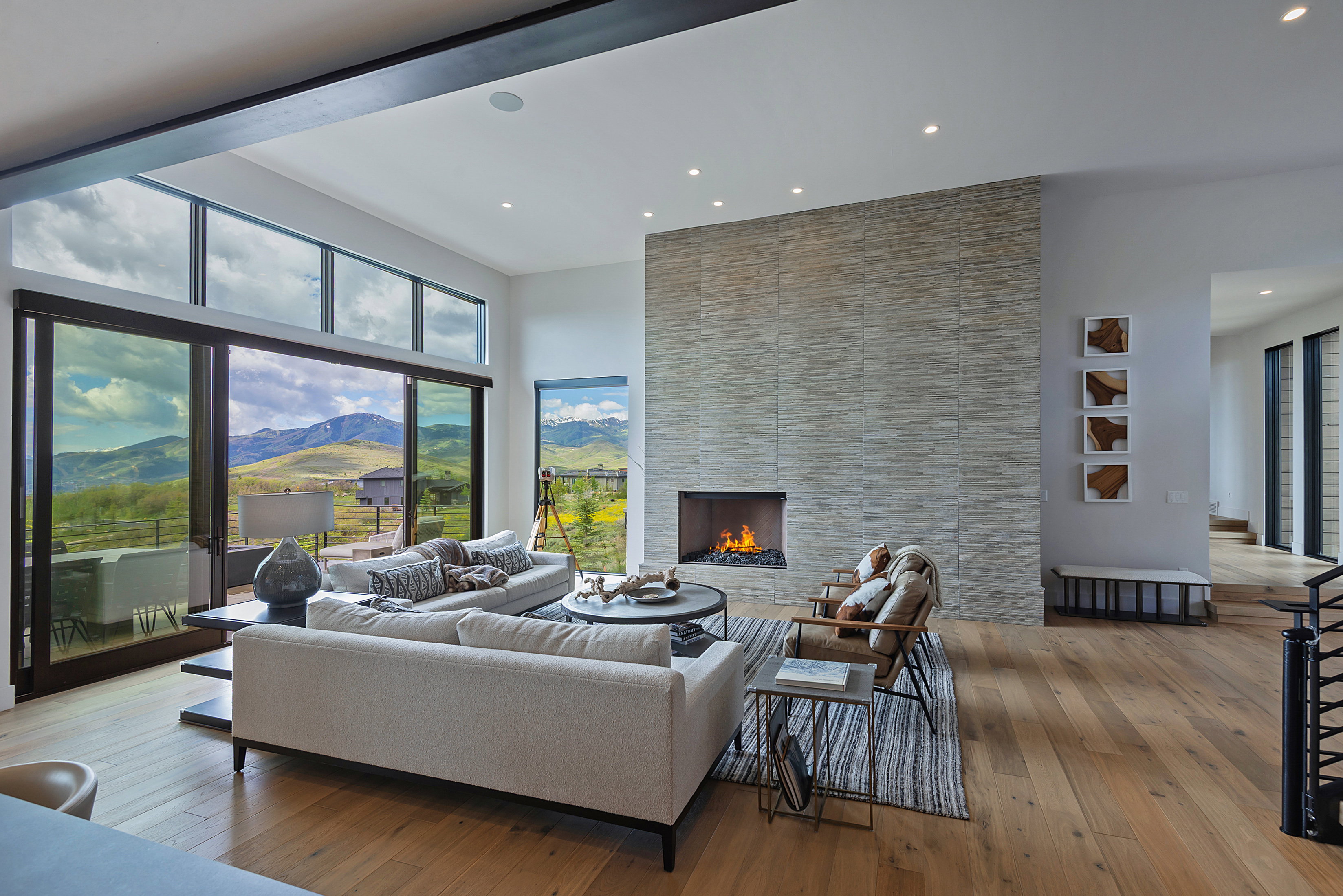 Contemporary living area featuring a floor-to-ceiling stacked stone fireplace with a gas insert, wide plank wood flooring, and extensive sliding glass doors