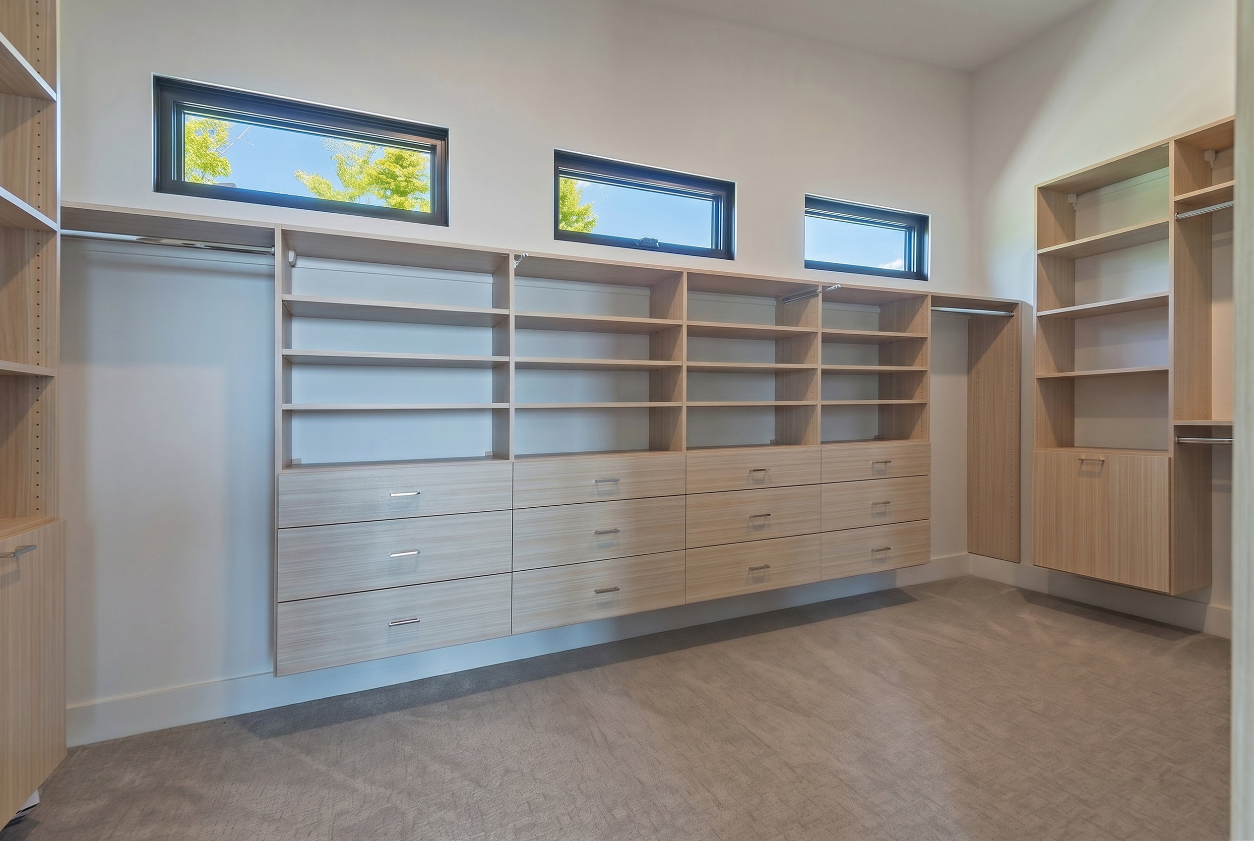 Custom closet system featuring extensive shelving, multiple integrated drawers with contemporary pulls, and dedicated hanging rods