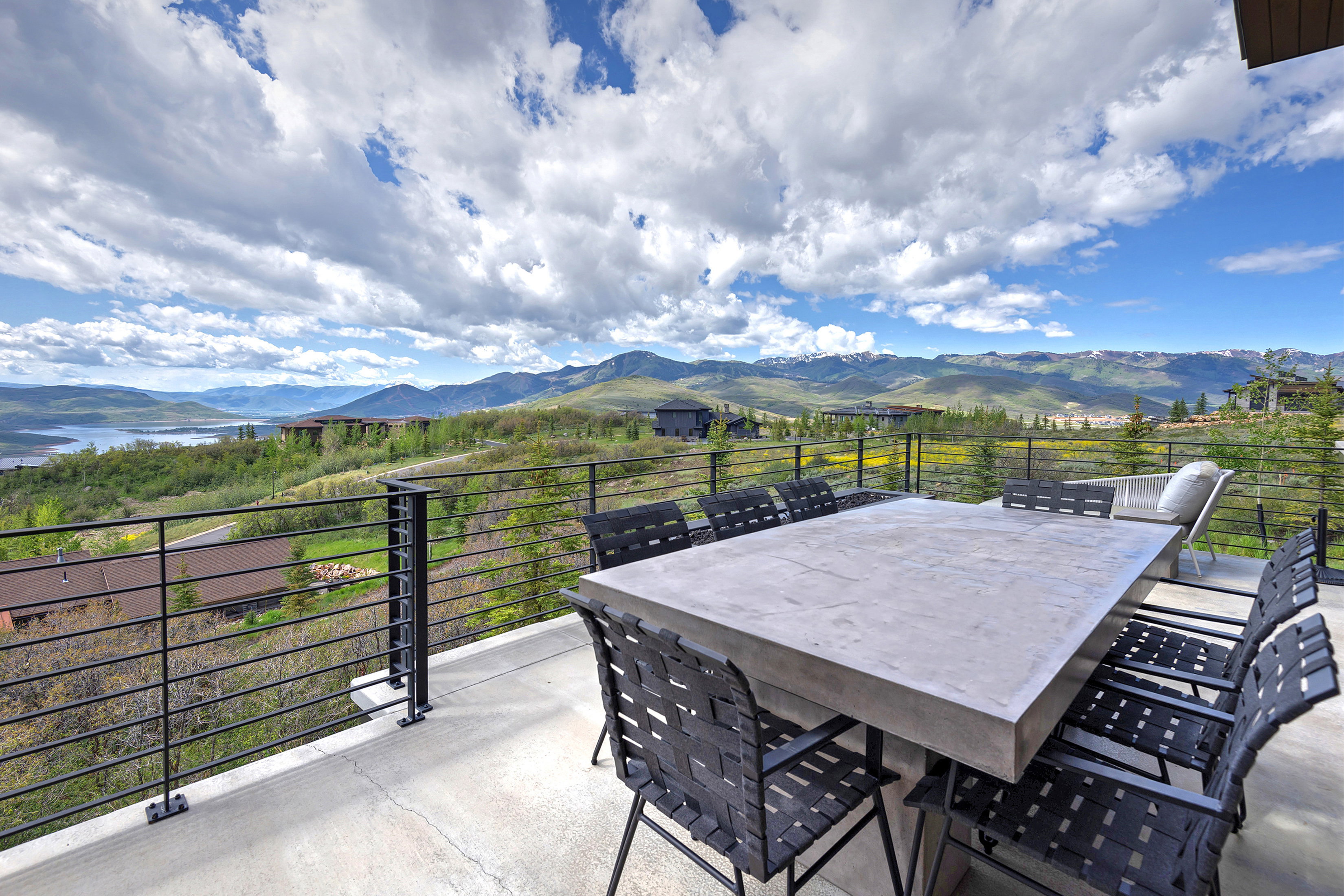 Outdoor patio featuring a concrete-finish surface, black horizontal cable railing, and expansive mountain and water scenery