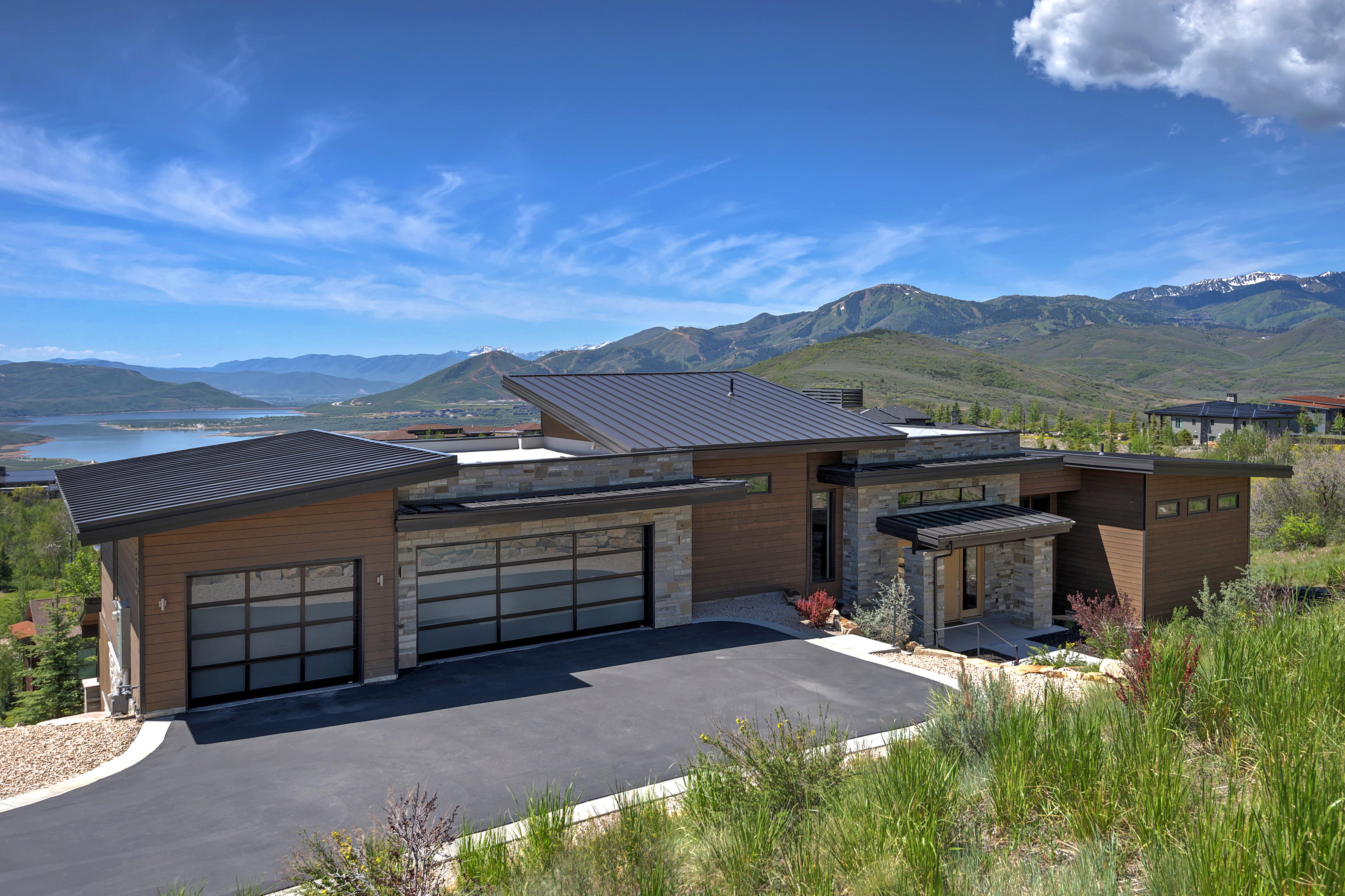 Modern residence featuring a metal roof, stone and wood-look siding, and a paved driveway