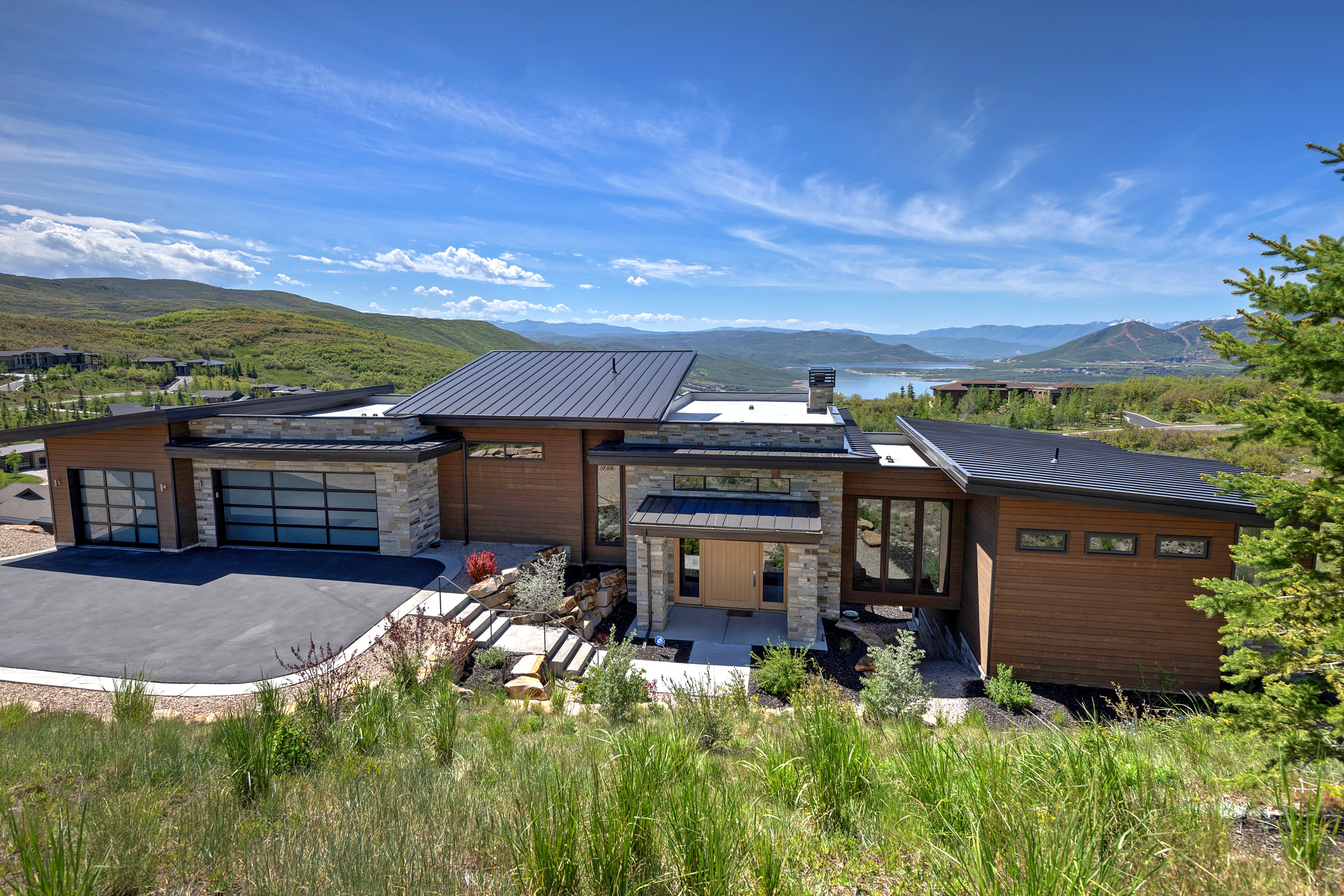 Modern architectural design featuring extensive wood paneling, stone accents, and a metal roof