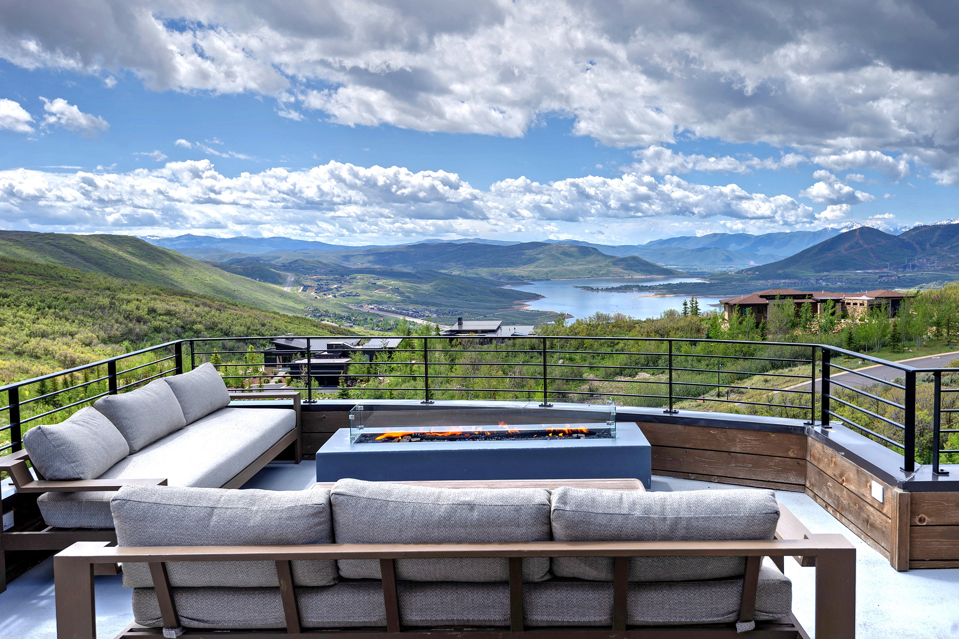 Expansive outdoor terrace featuring a built-in fire pit, metal railings, and wood-finish accent walls