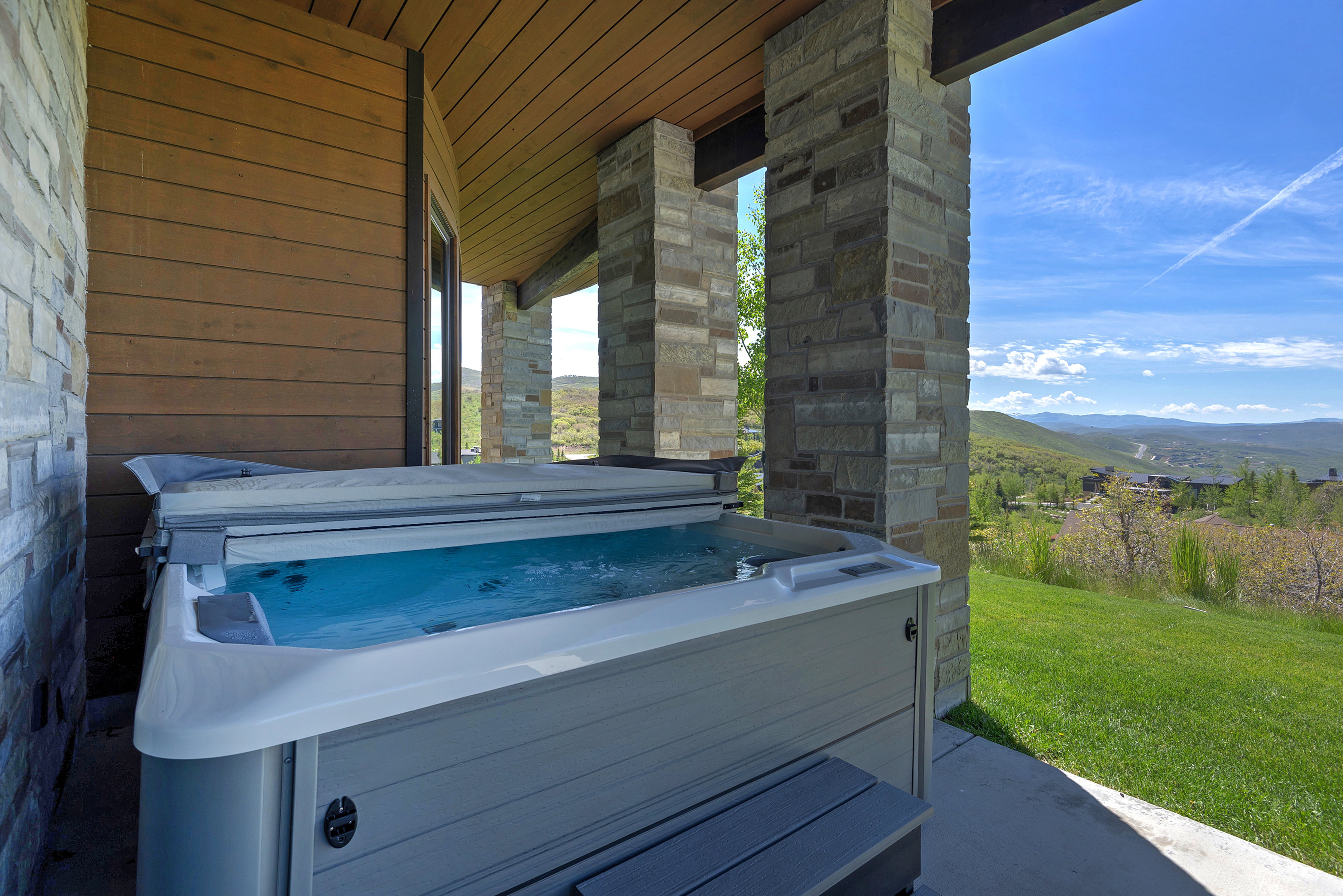 Covered patio featuring a built-in spa, stone columns, wood-paneled ceiling, and a concrete patio surface