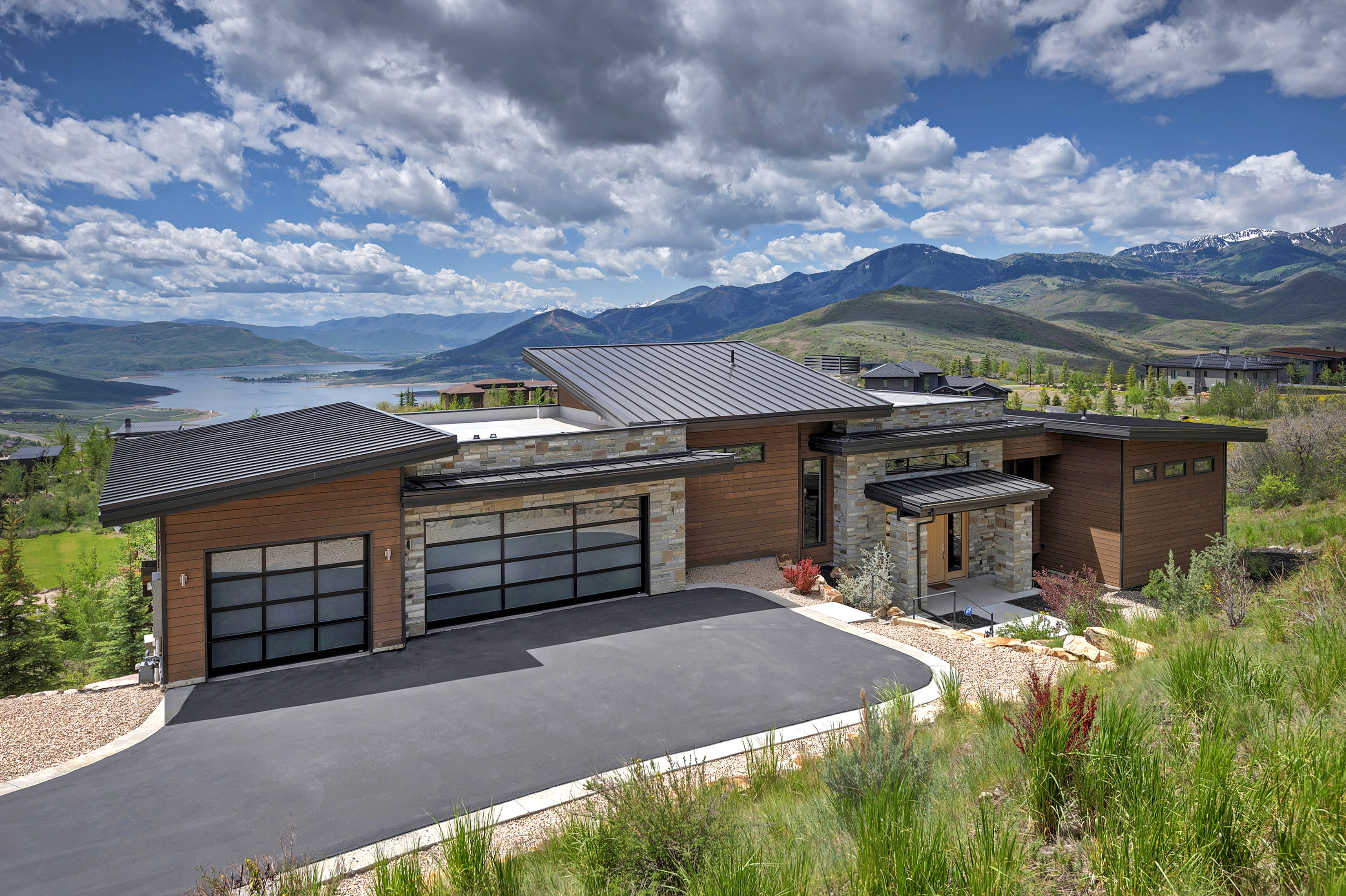 Modern architectural exterior featuring wood-finish siding, stone accents, and a metal roof