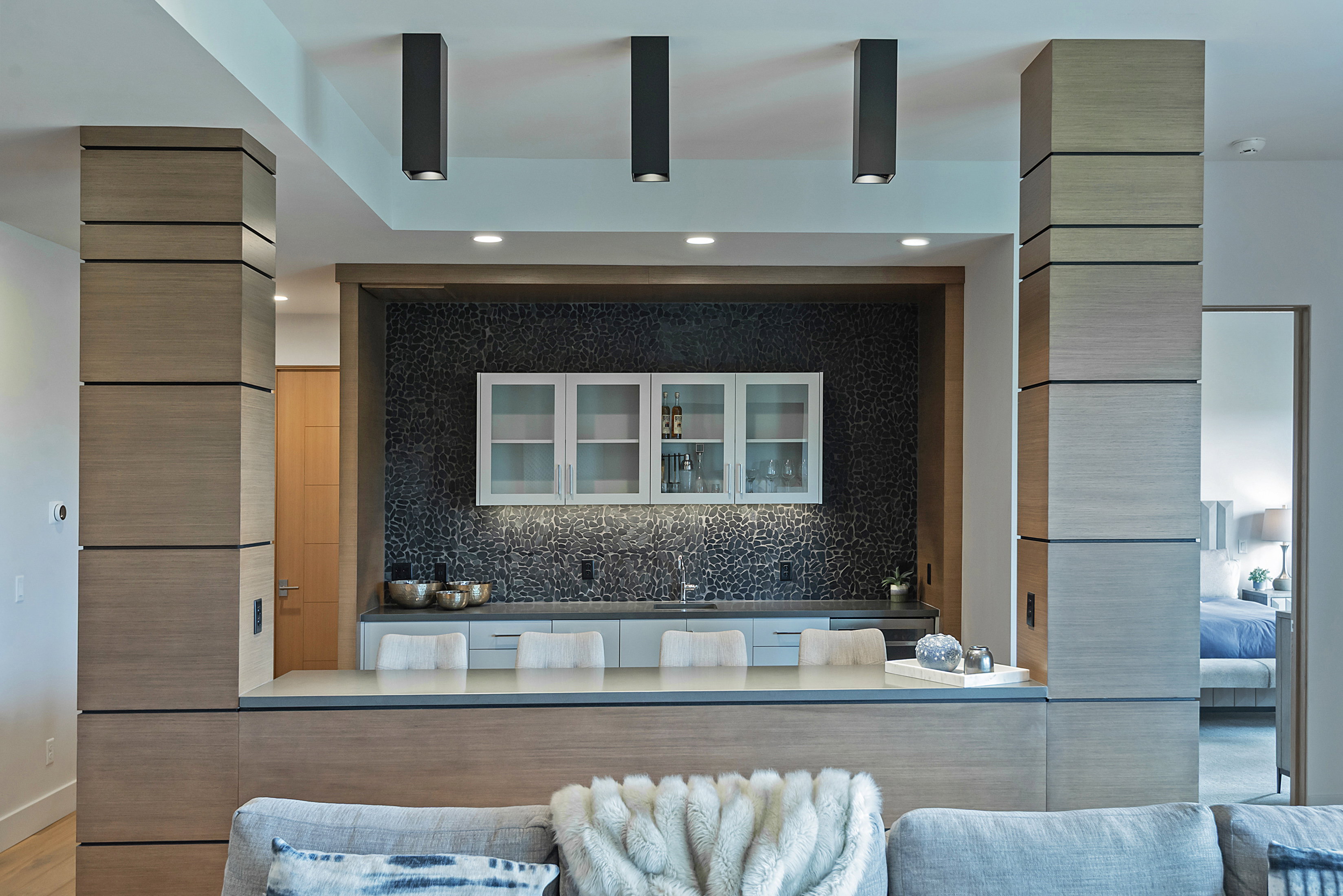 Integrated wet bar featuring a mosaic tile backsplash, under-cabinet lighting, and white upper cabinetry with glass inserts