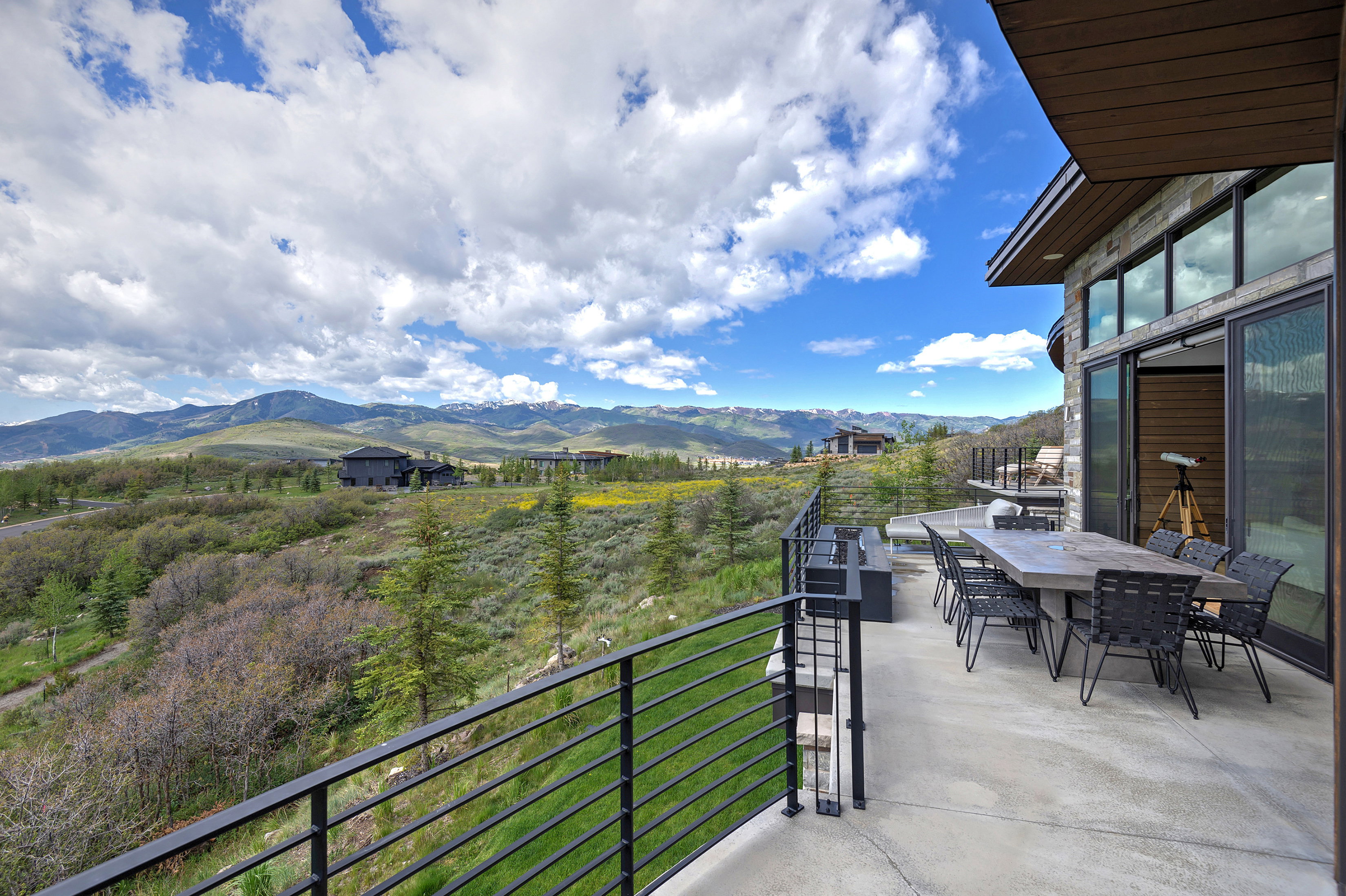 Expansive outdoor terrace featuring panoramic mountain scenery, concrete flooring, a modern horizontal railing system, and a built-in outdoor fireplace