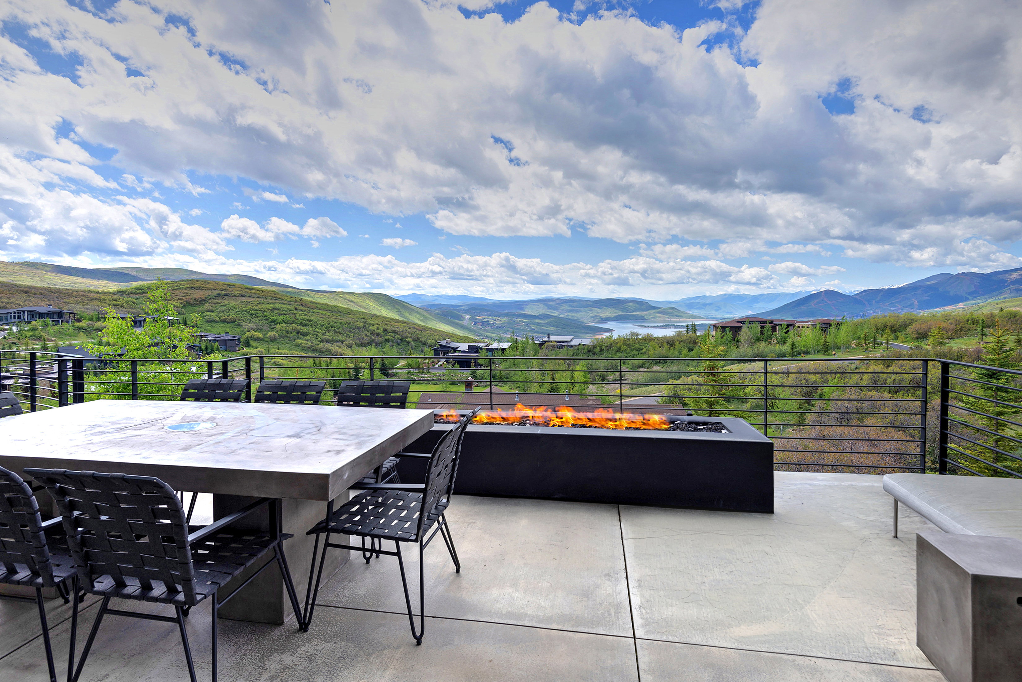 Expansive outdoor patio featuring a linear gas fire pit, concrete dining table, and a horizontal bar railing system