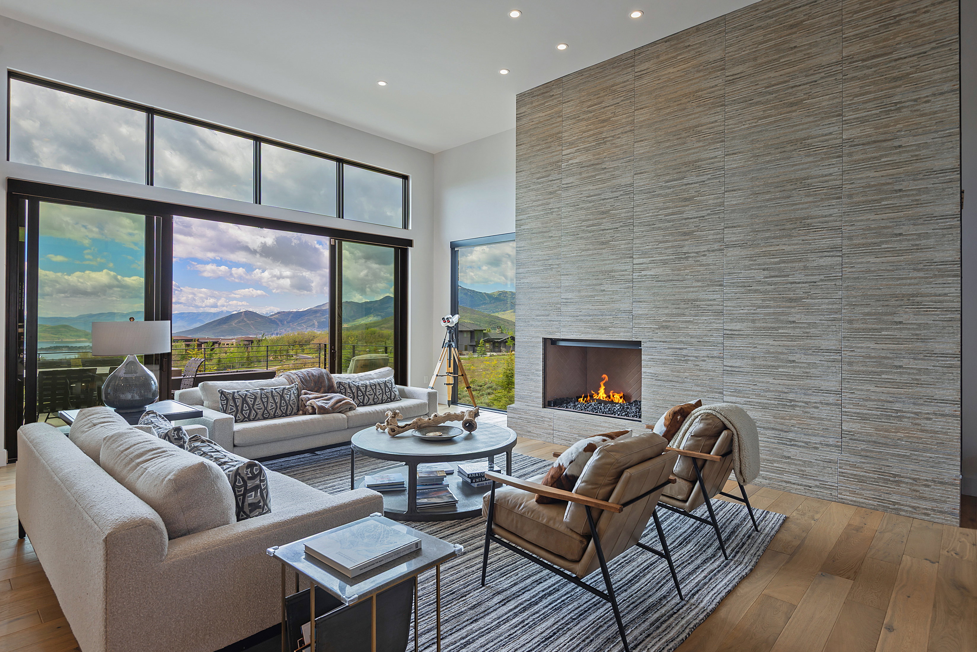 Spacious living area featuring large format sliding glass doors, upper transom windows, a floor-to-ceiling textured tile fireplace, recessed lighting, and wood-finish flooring