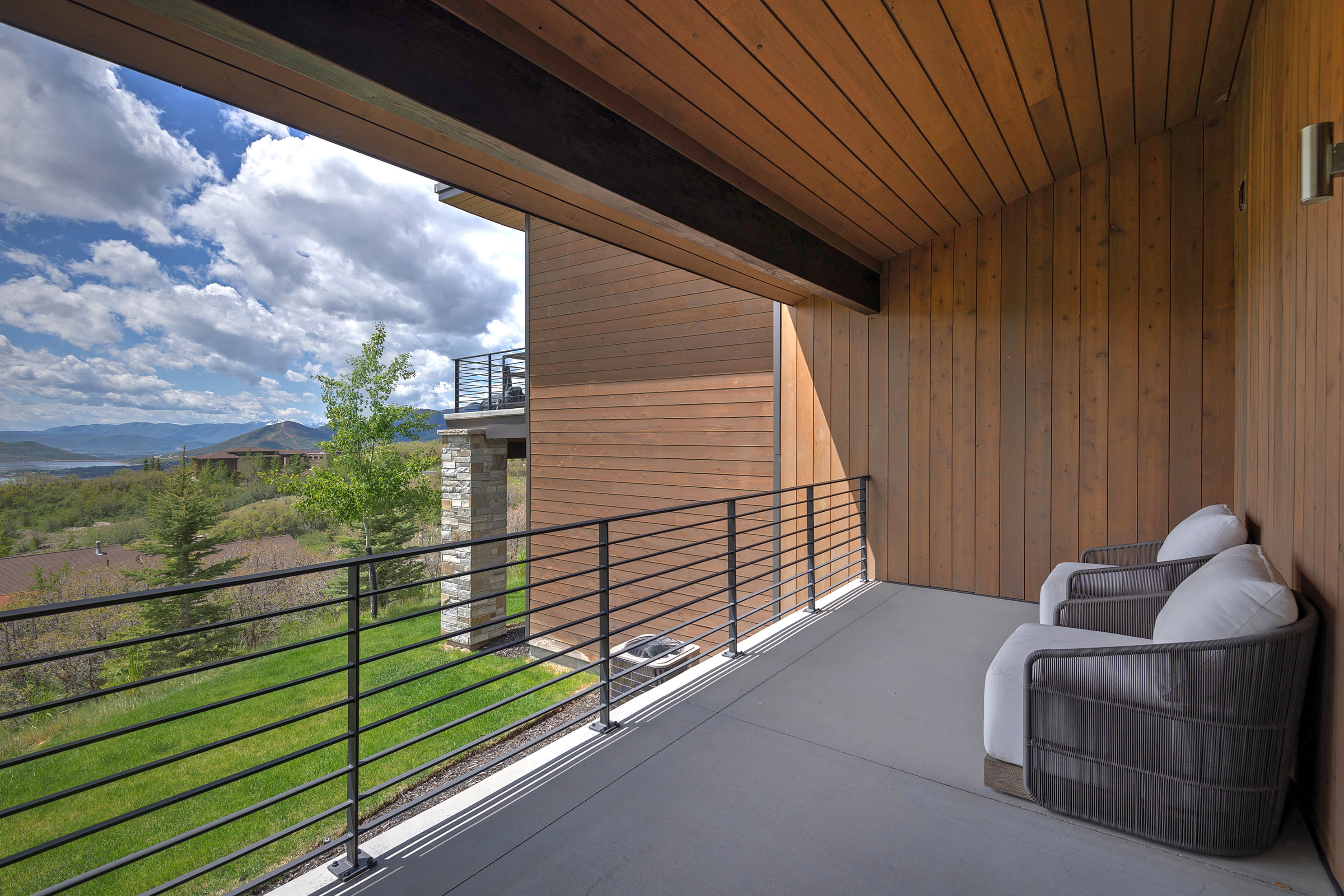 Covered balcony featuring wood-finish ceiling and wall paneling, a dark gray floor, and a black metal railing