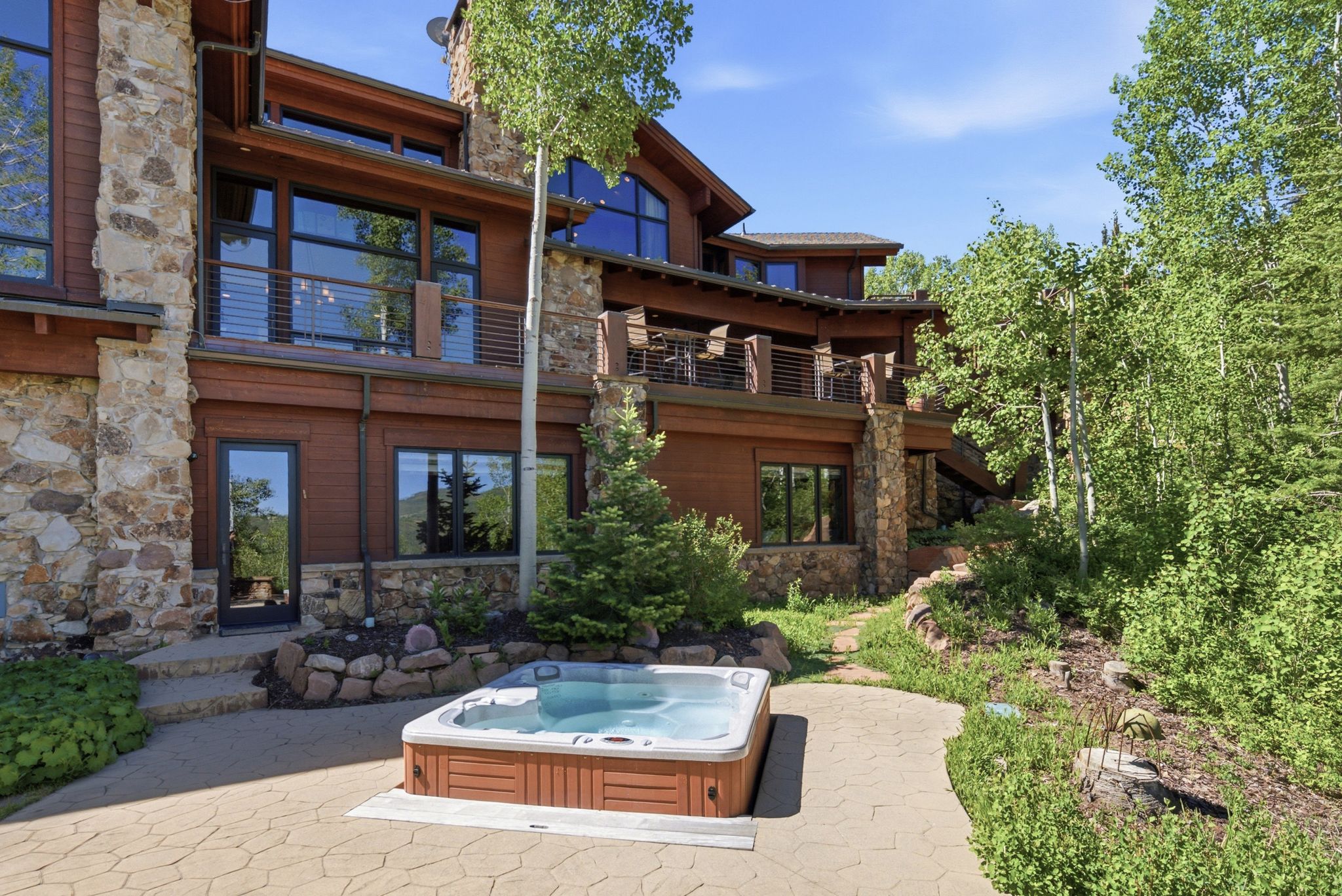 Outdoor hot tub on a stamped concrete patio, surrounded by mature trees
