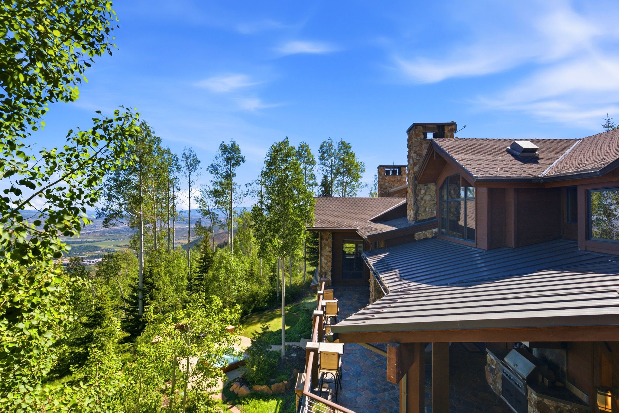 Multi-level residence featuring a brown shingle roof, stone chimneys, and dark-stained exterior siding