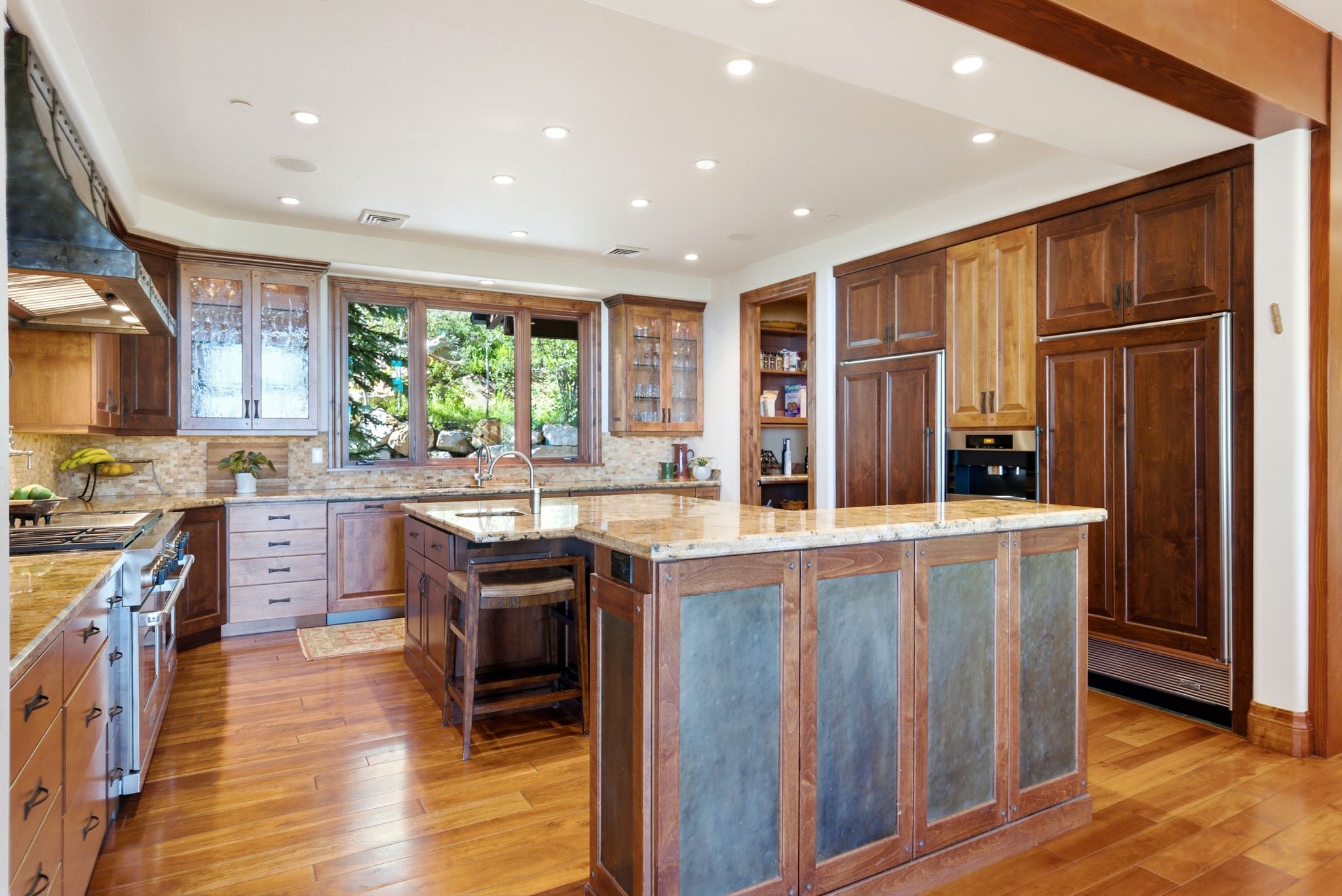 Spacious kitchen featuring a large central island with a stone countertop, wood-finish flooring, recessed lighting, custom cabinetry, and built-in stainless steel appliances