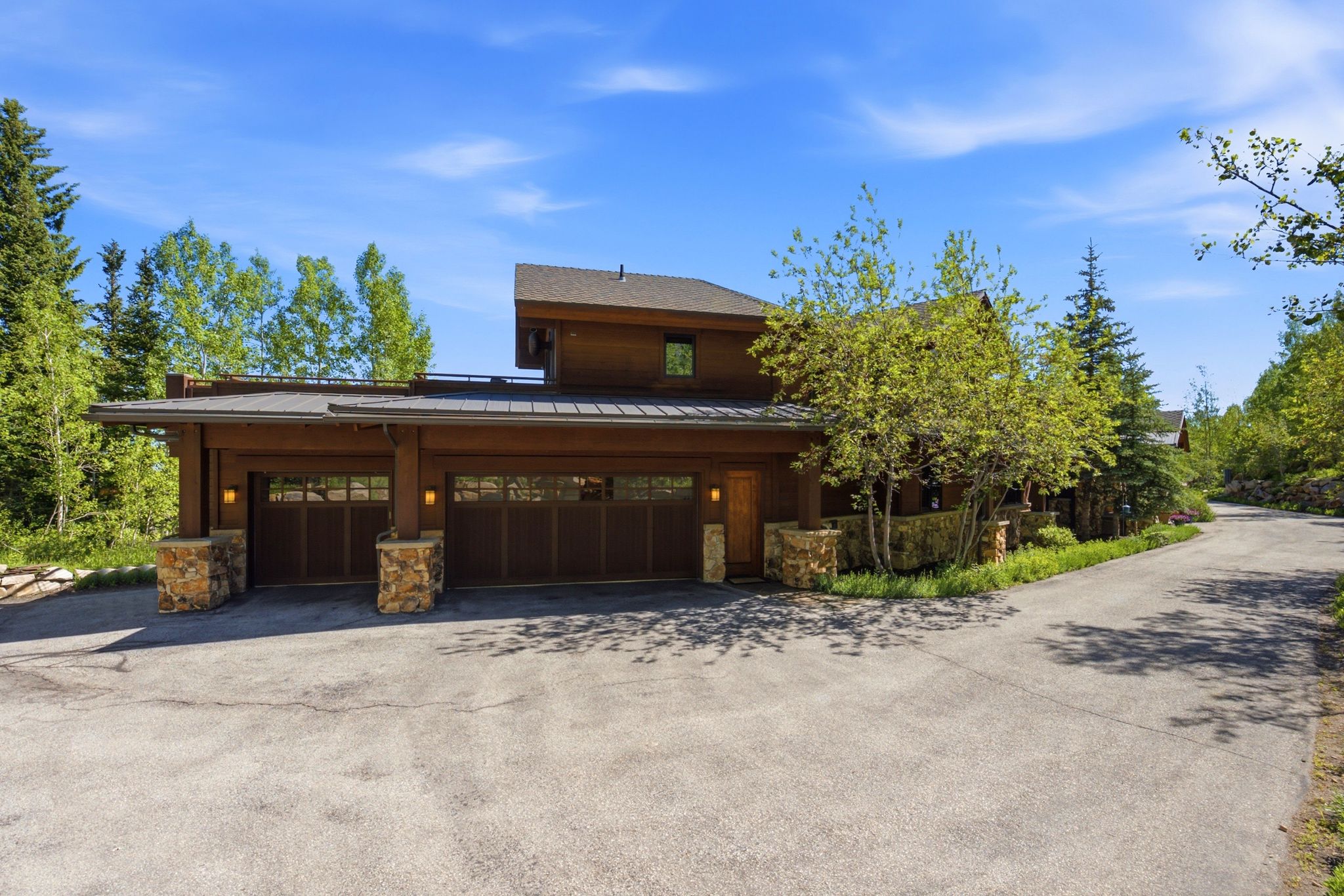 Rustic modern architecture featuring wood siding, stone pillar accents, and a multi-car garage with overhead lighting