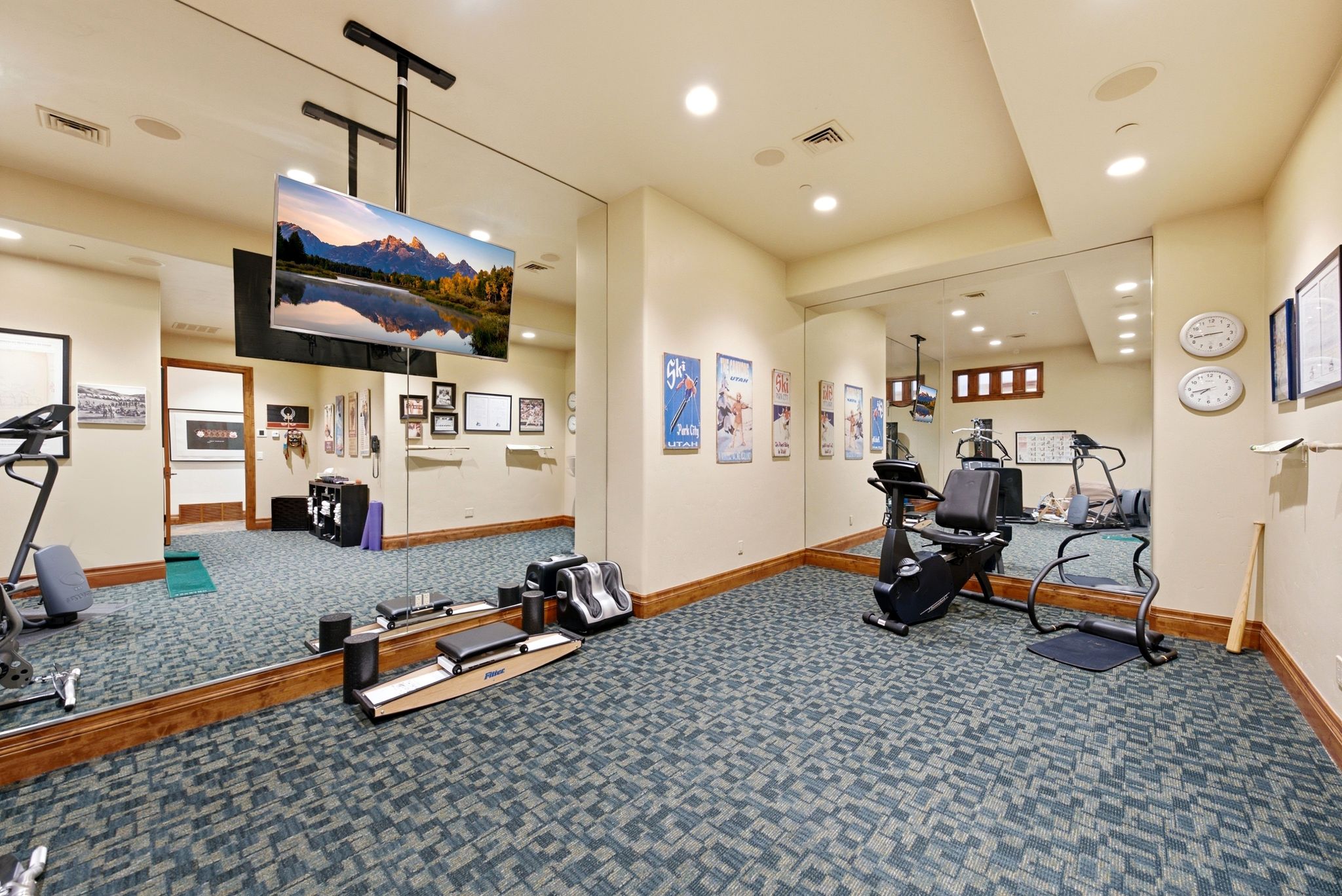 Dedicated fitness space featuring wall-mounted mirrors, recessed lighting, ceiling-mounted television, and patterned carpet flooring with wood baseboards