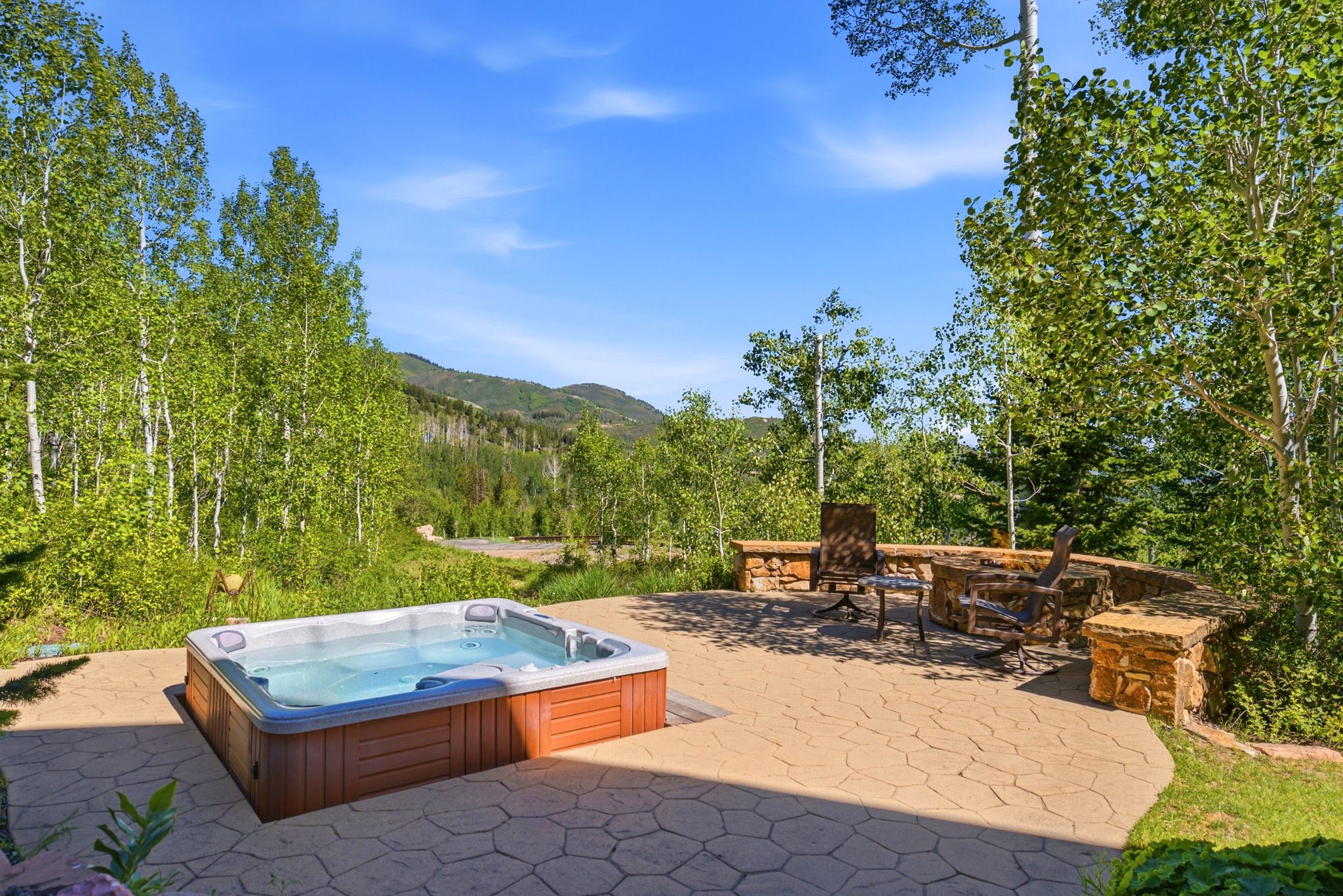 Outdoor patio featuring a built-in hot tub, stamped concrete paving, and a stone-built fire pit area