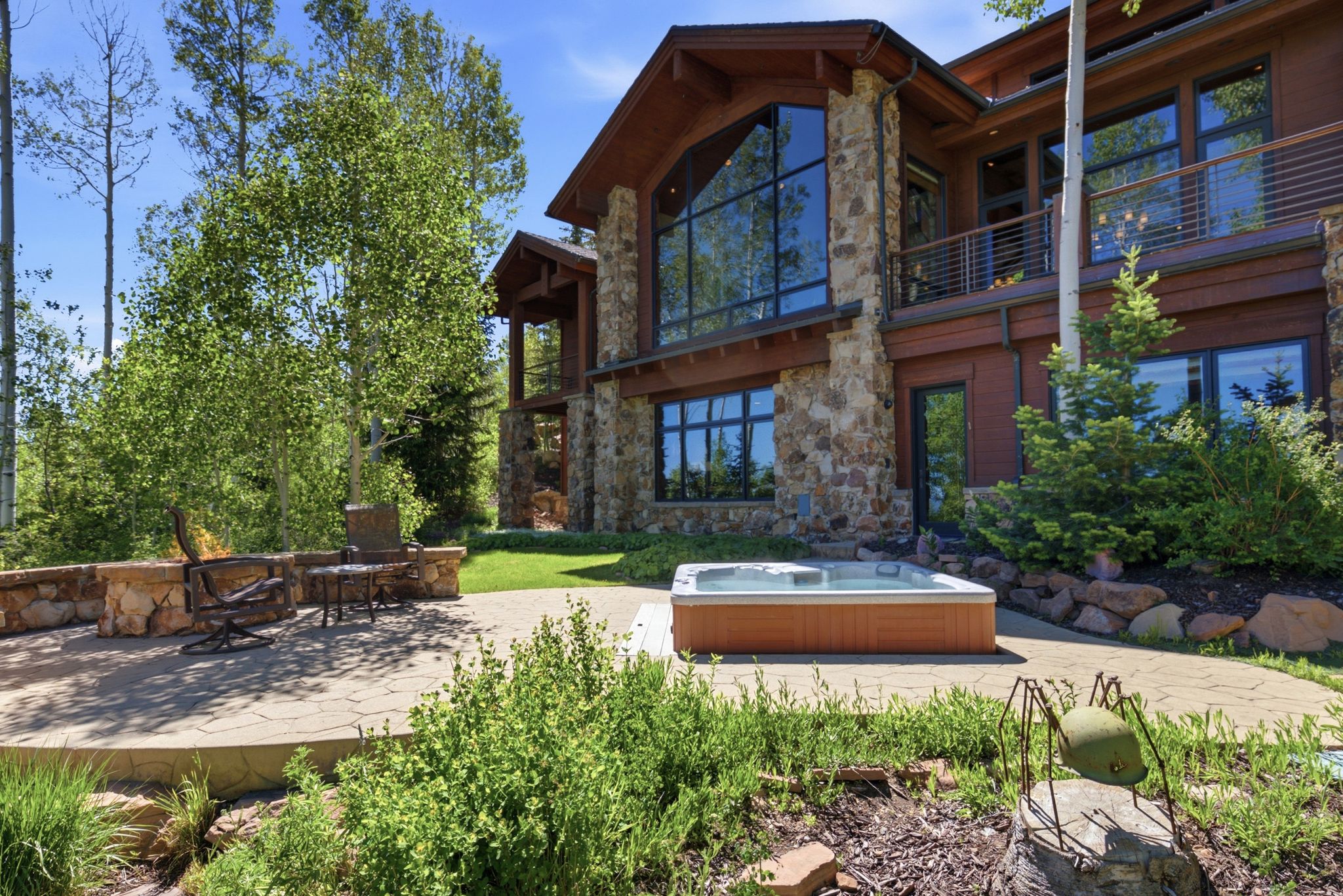 Expansive stone patio featuring a built-in hot tub, surrounded by mature trees and natural landscaping