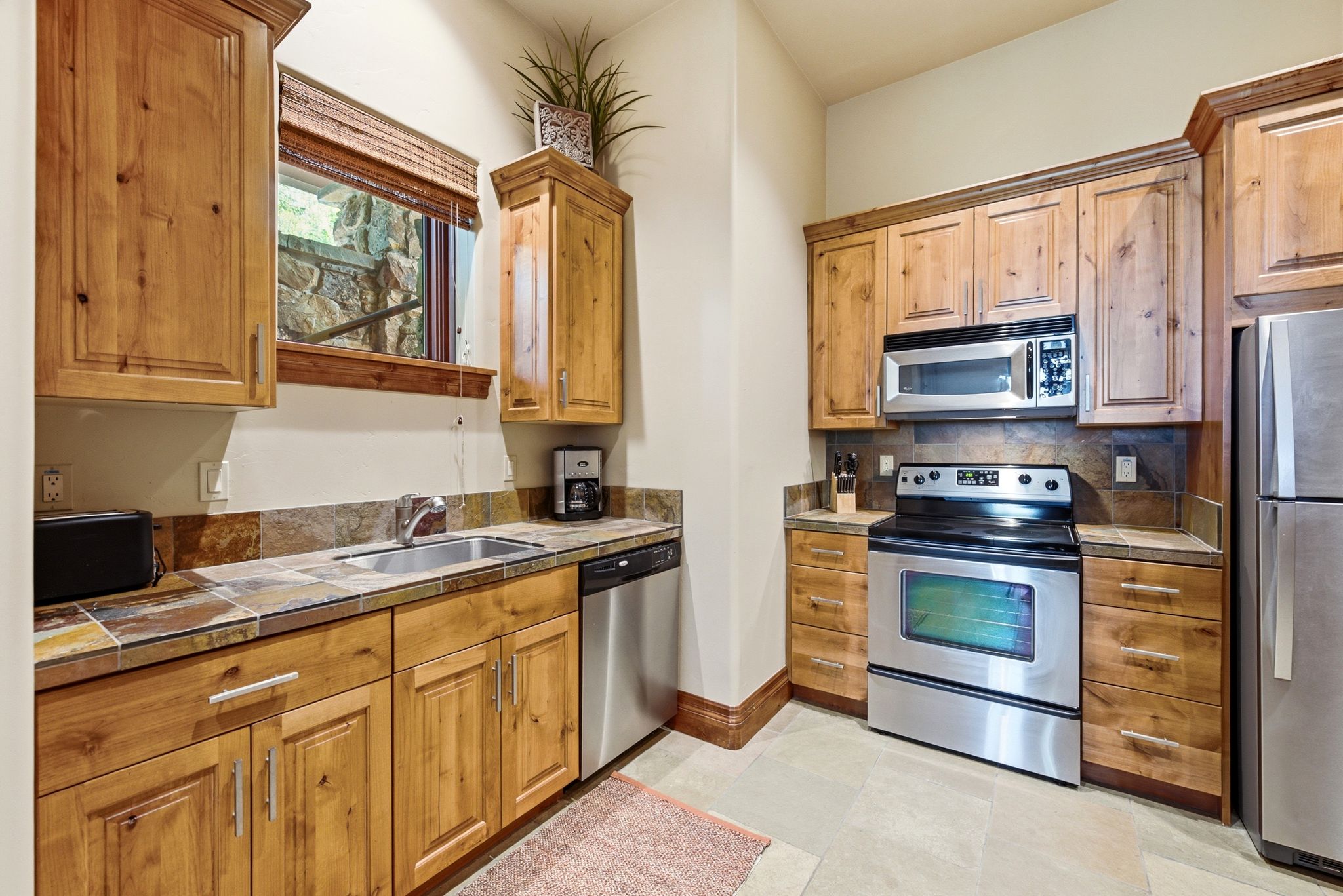 Kitchen featuring wood cabinetry, stainless steel appliances, tile countertops, and a tile backsplash