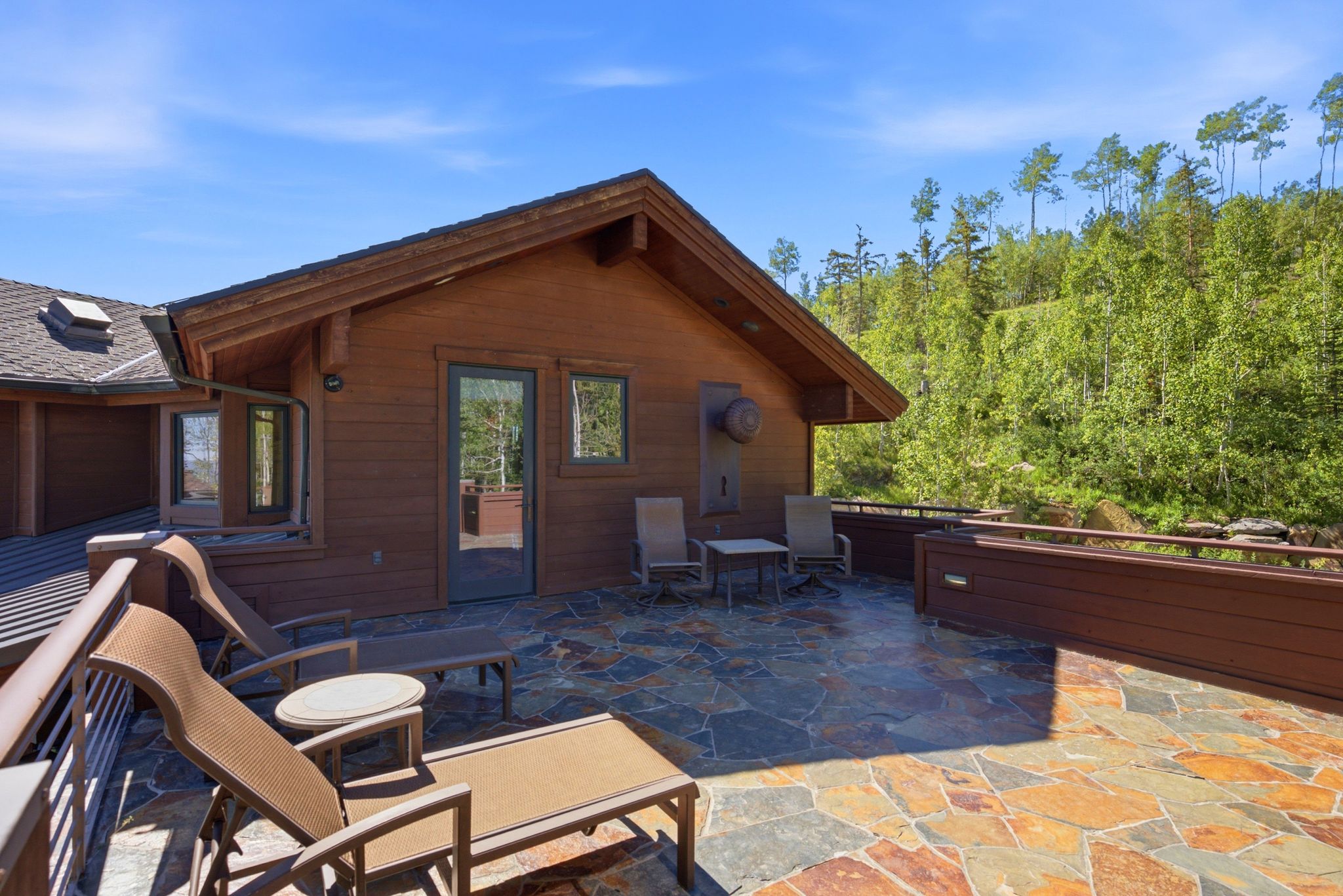 Expansive stone patio with wood siding and a natural tree-lined backdrop