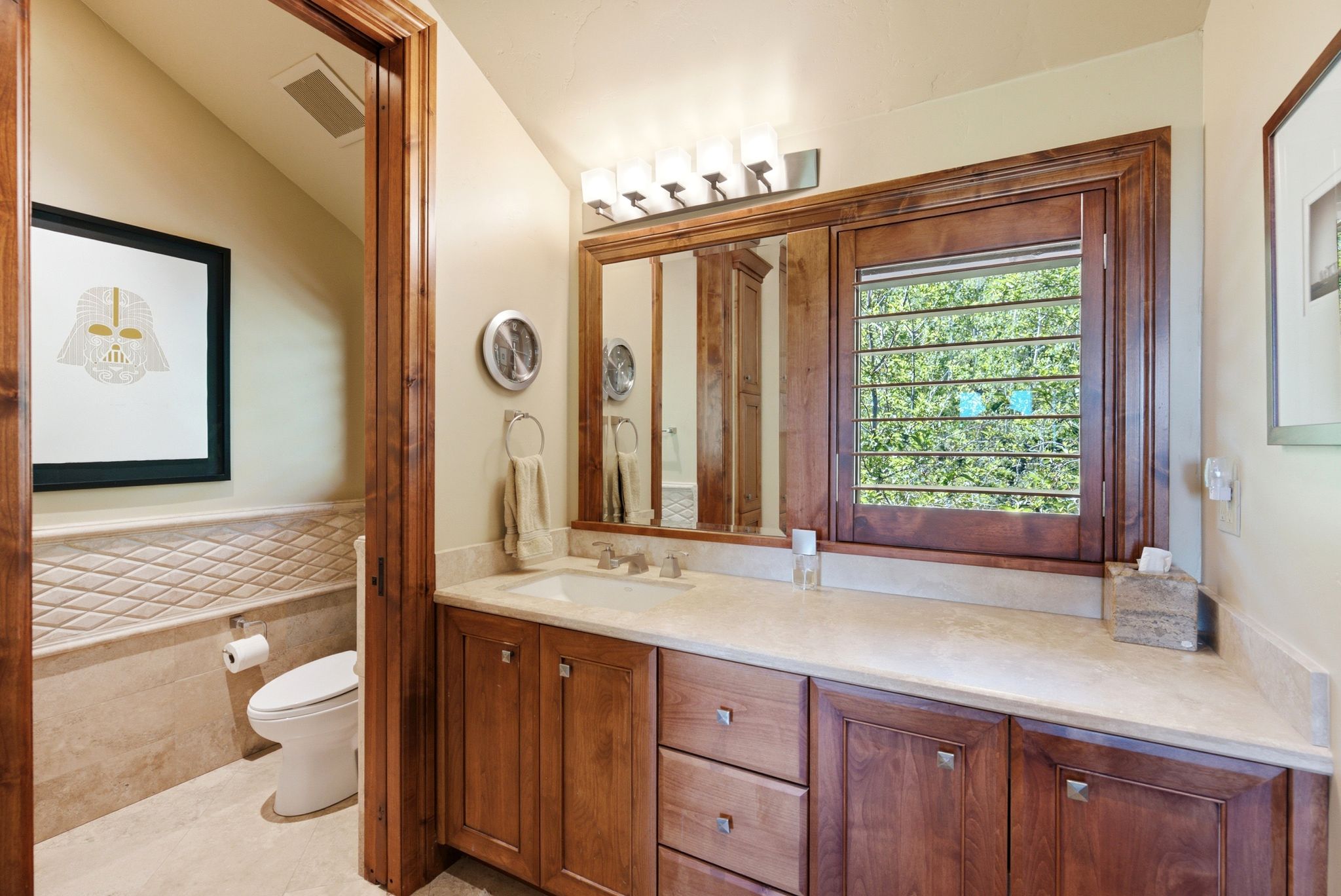 Bathroom featuring a single vanity with wood cabinetry and a light-toned countertop, framed mirror, and a window with wood shutters