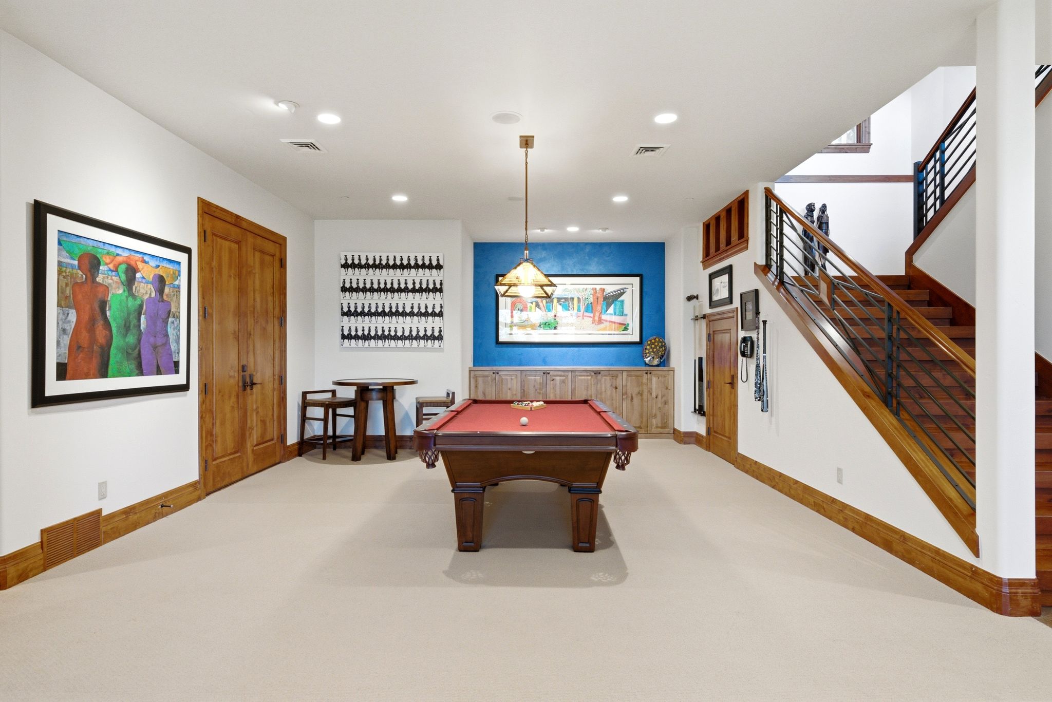 Spacious recreation room featuring a central billiards table, light neutral carpeting, and a contrasting blue accent wall