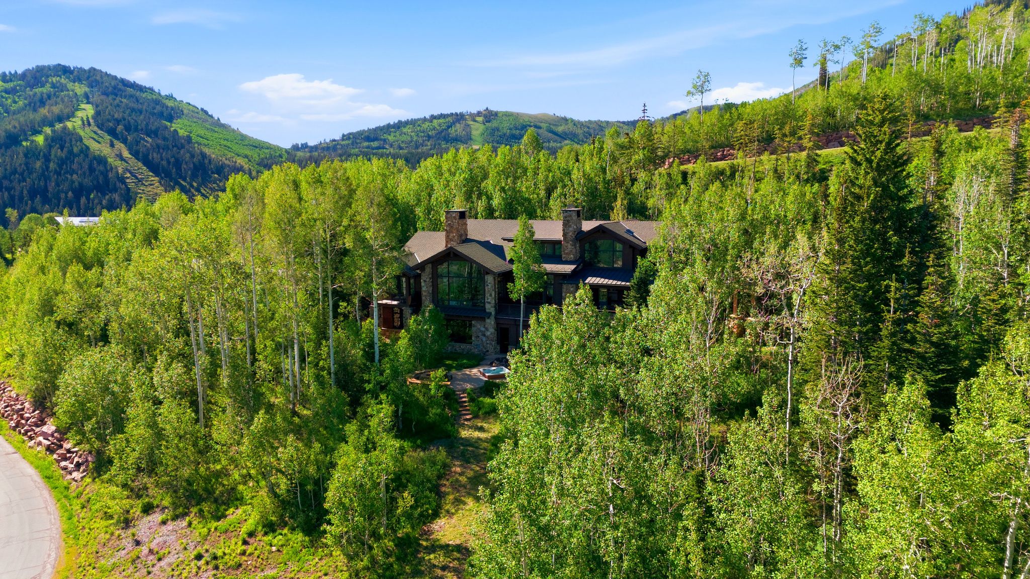 Stone and wood-clad residence nestled among abundant trees, featuring multiple chimneys, a multi-pane window, and a visible hot tub