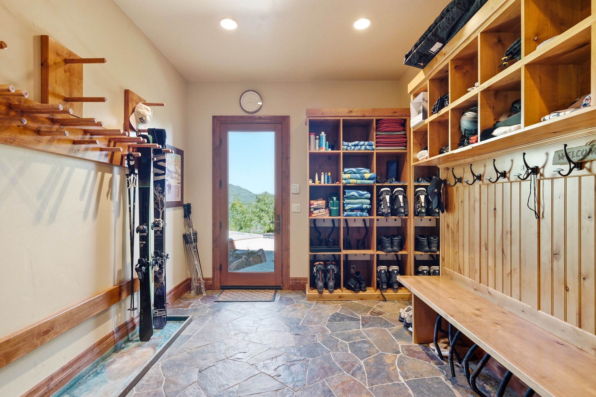 Mudroom featuring natural stone flooring, a full-lite exterior door, built-in wooden storage cubbies, a dedicated ski and boot drying system, and a built-in wooden bench with coat hooks