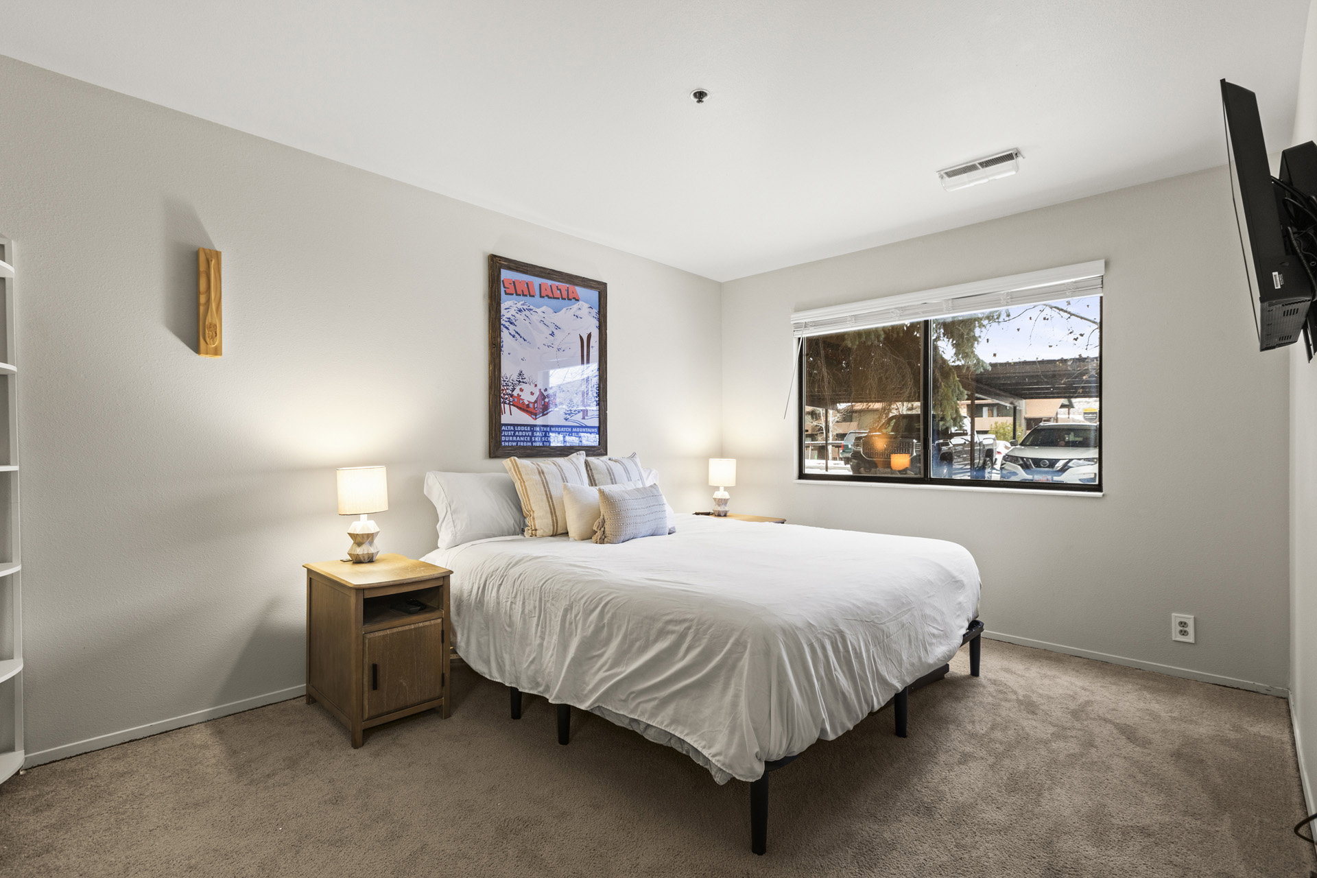 Bedroom featuring a large window with roller shades, light grey wall paint, and tan carpet flooring
