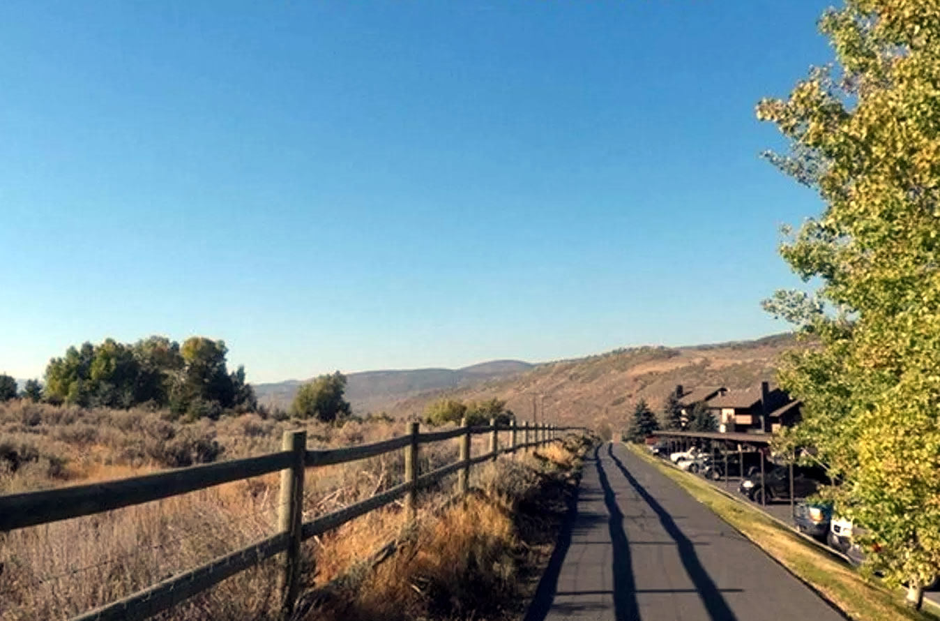 Paved pathway bordered by a rustic wooden fence and natural landscaping