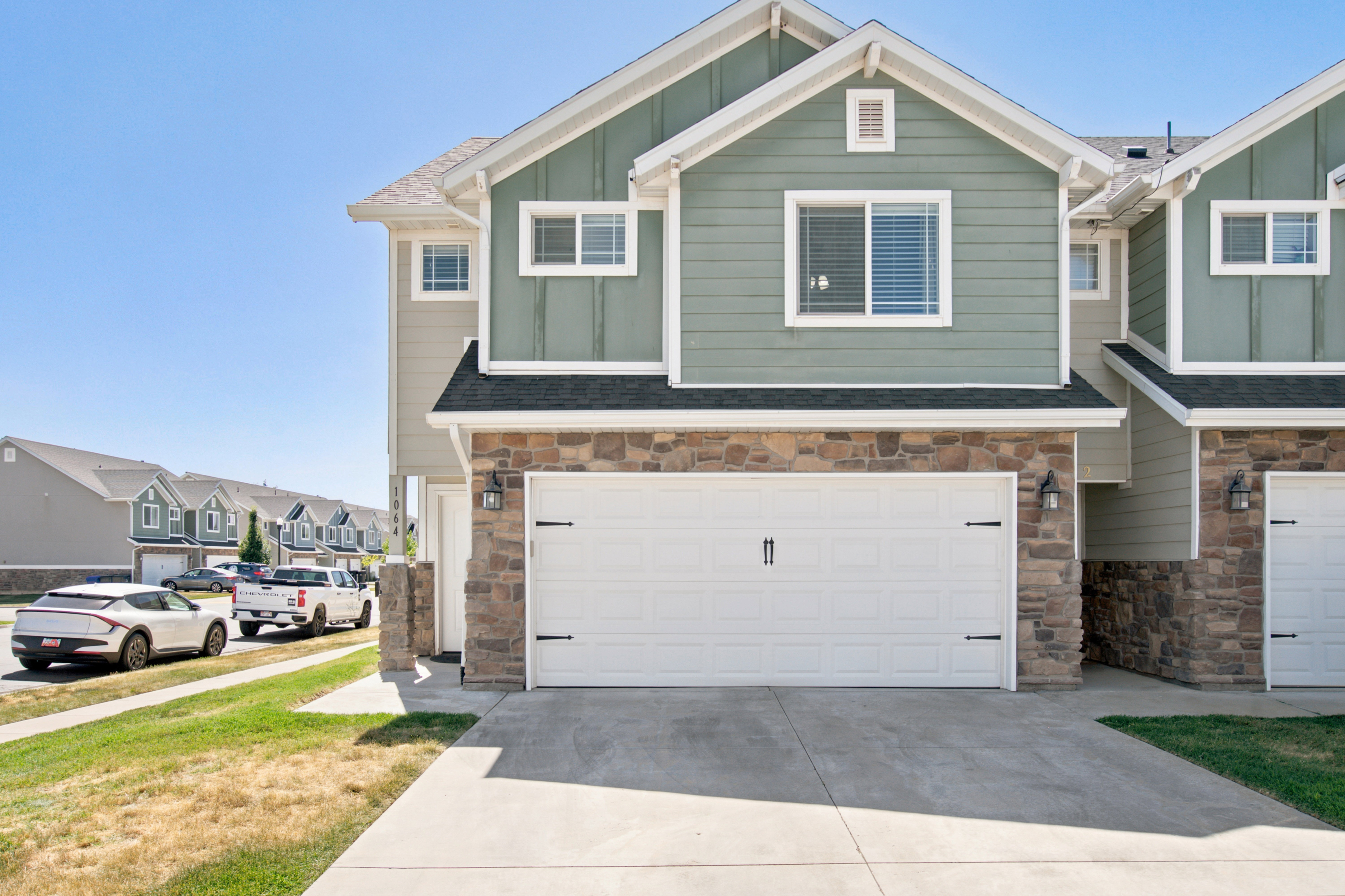 Contemporary townhouse exterior featuring a two-car garage, stone veneer siding, green horizontal siding, and white trim accents
