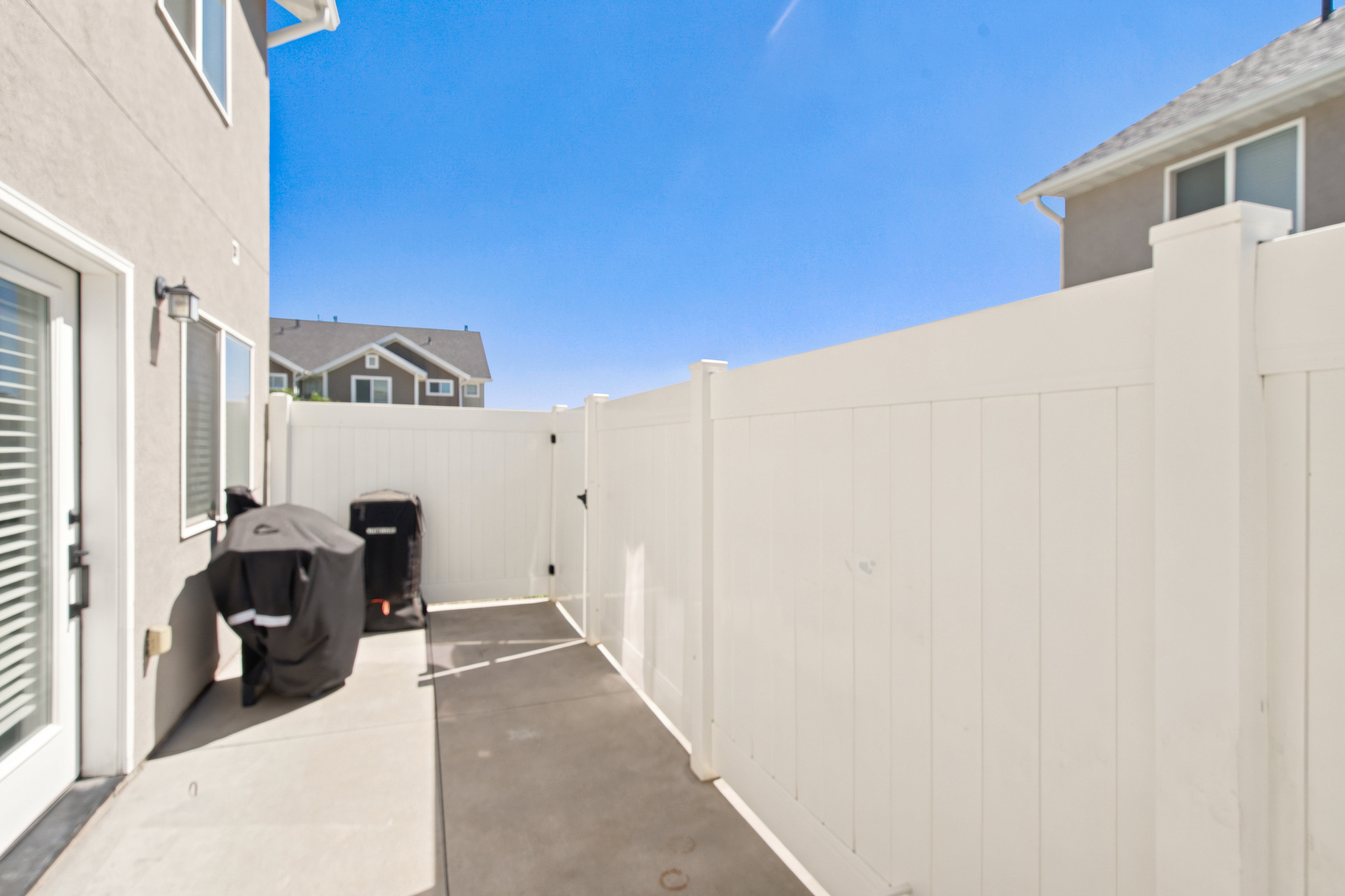 Private outdoor patio featuring a concrete surface, white privacy fencing, and exterior wall-mounted lighting fixtures
