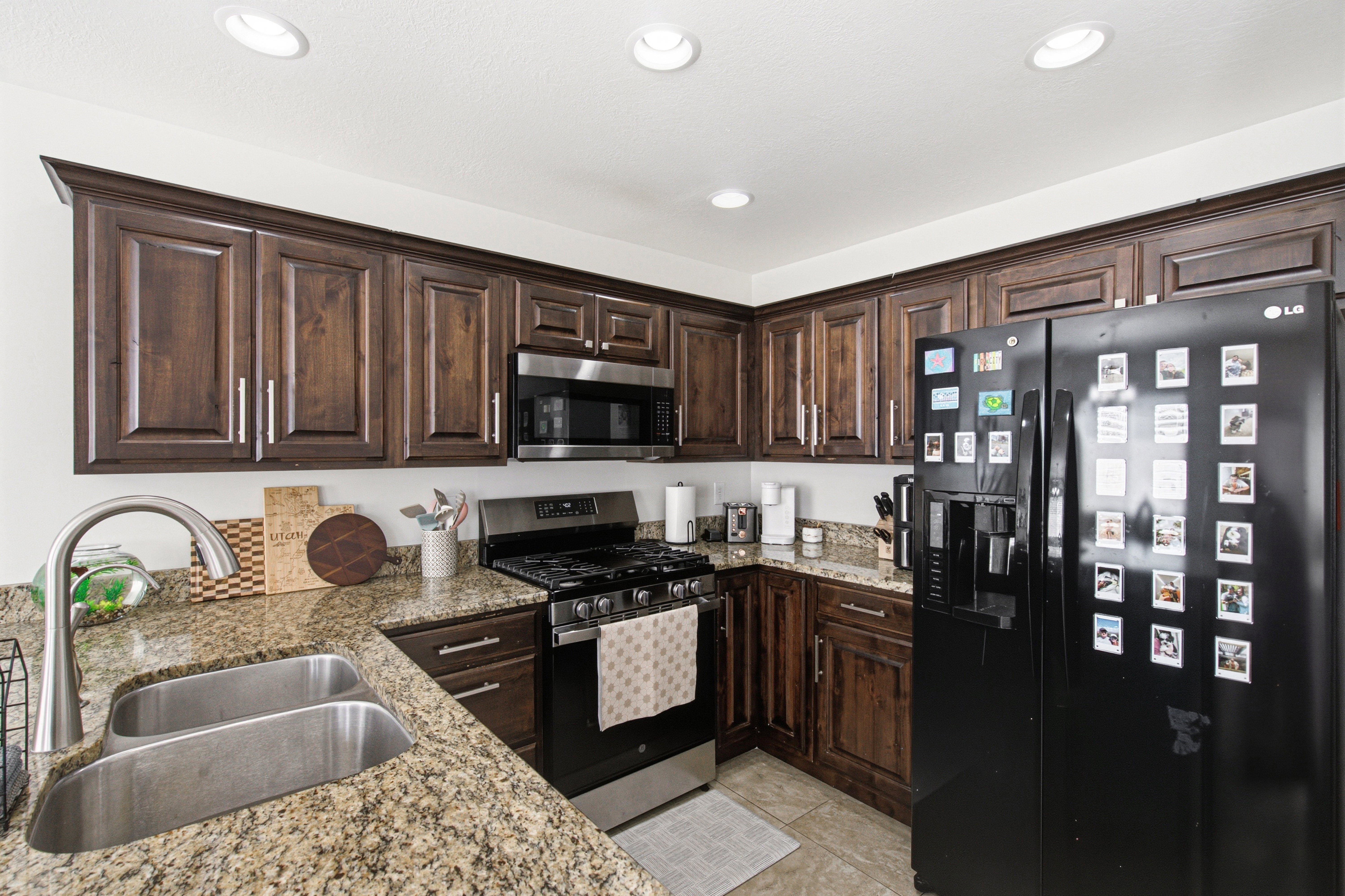 Kitchen featuring rich wood cabinetry with crown molding, granite countertops, a double basin stainless steel sink with a gooseneck faucet, a stainless steel microwave, and a black gas range