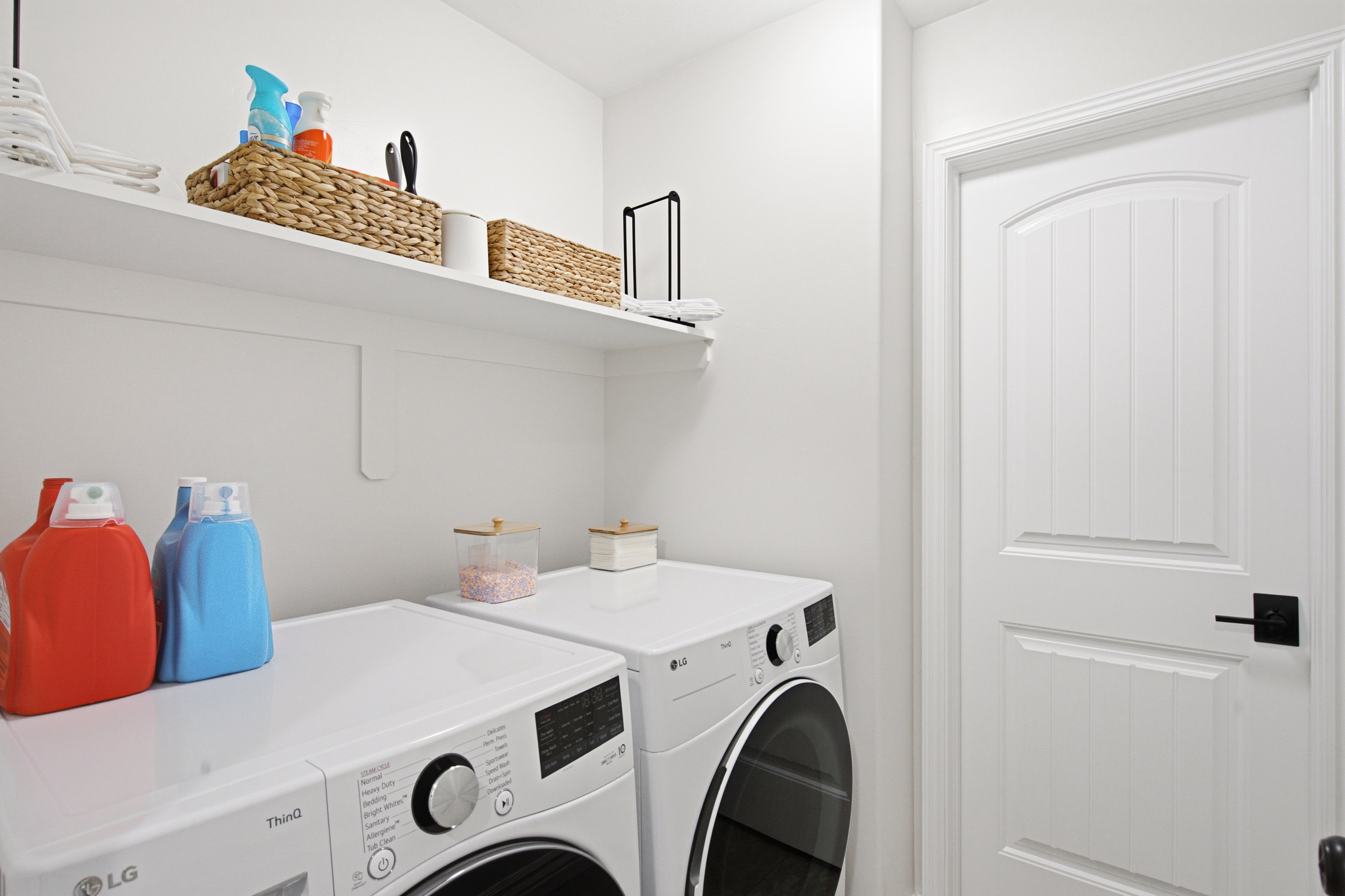 Laundry space featuring wall-mounted shelving, white appliances, and a paneled door with black hardware