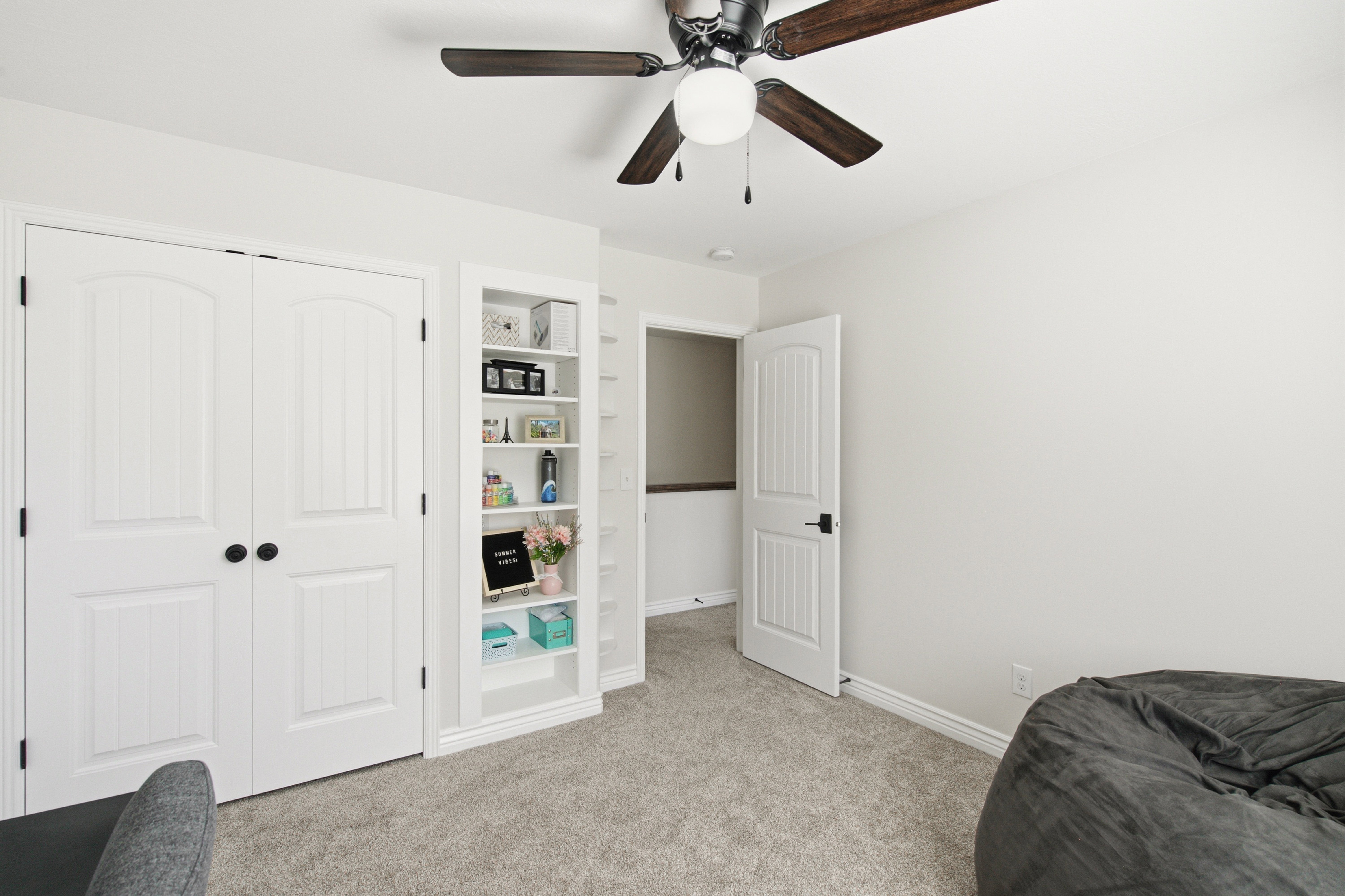 White interior featuring carpet flooring, built-in shelving, a ceiling fan with light fixture, and arched panel doors with matte black hardware