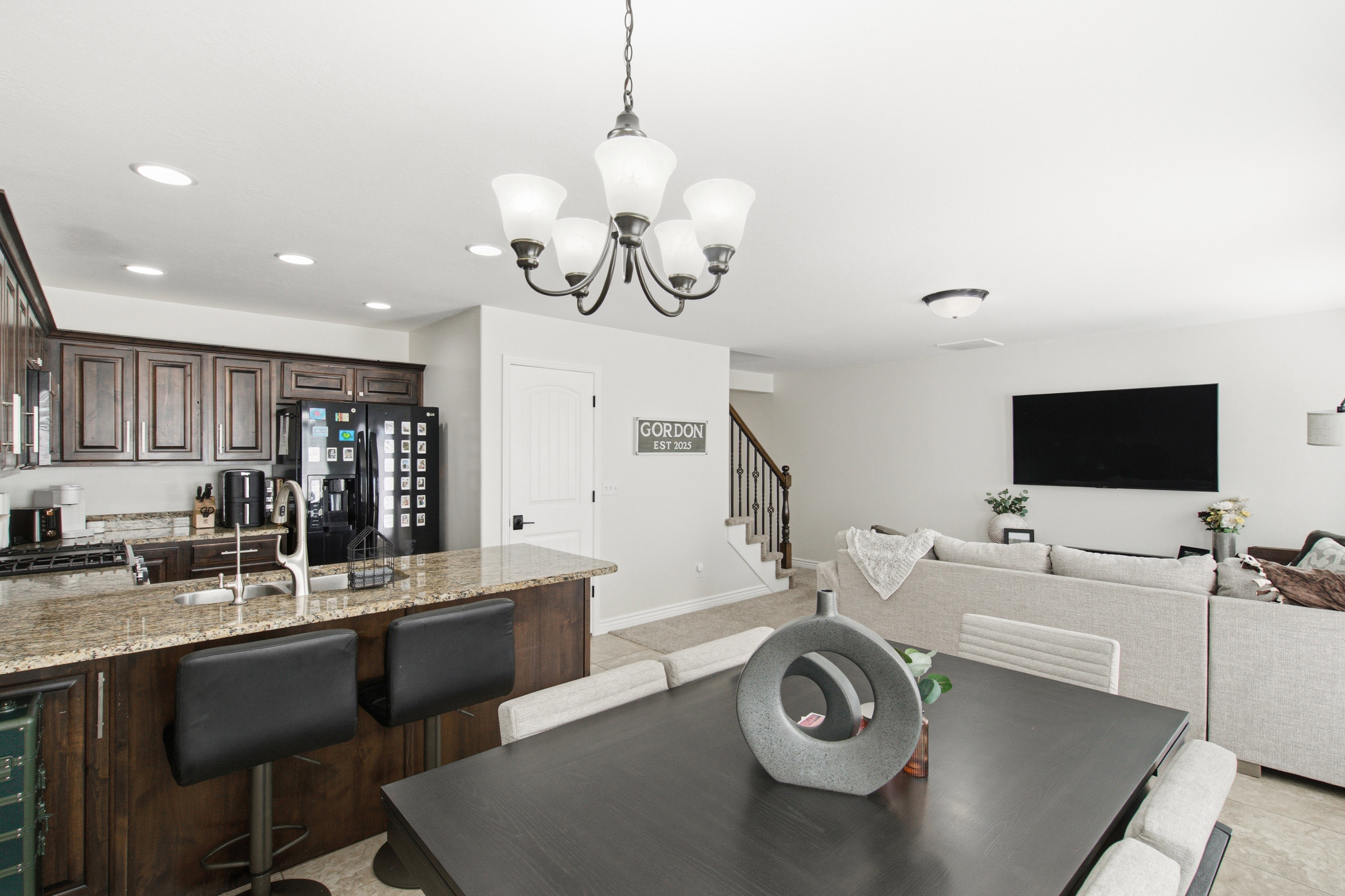 Open-concept living space featuring a kitchen with dark wood cabinetry and granite countertops, a dining area with a chandelier, and a living room
