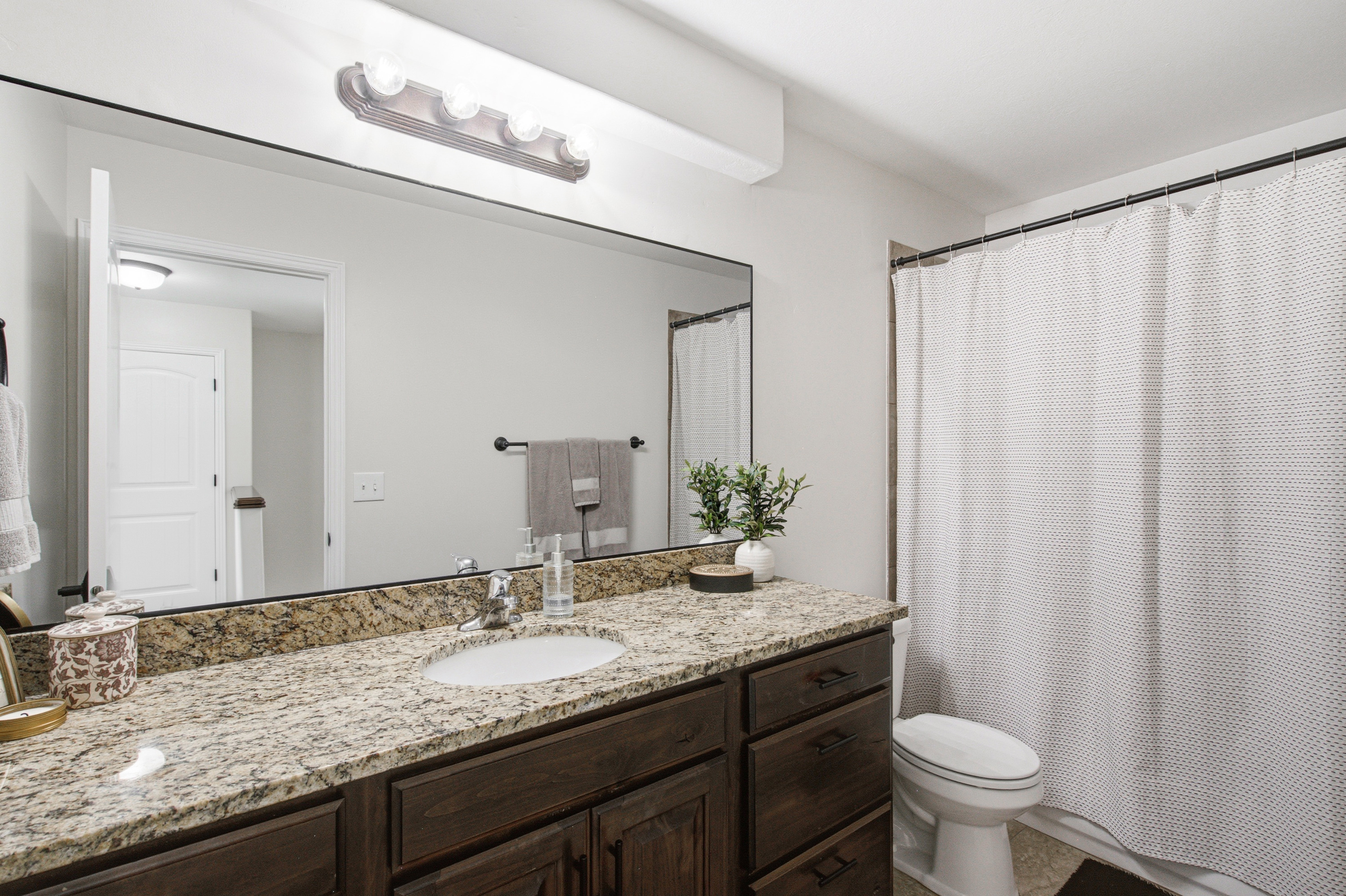 Bathroom featuring a dark wood-finish vanity with an undermount sink, a flecked stone countertop, and a large wall-mounted mirror