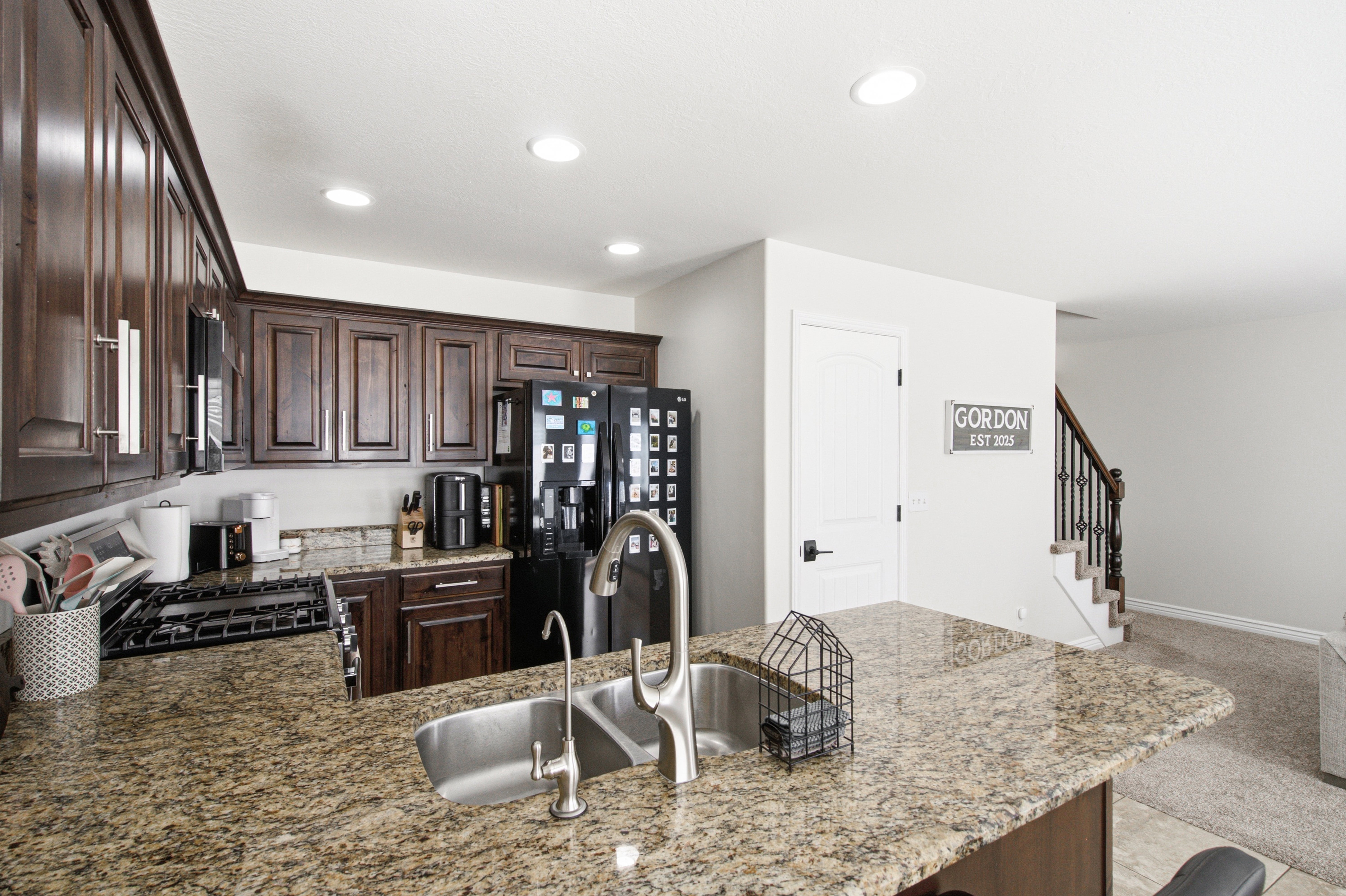 Kitchen featuring granite countertops, dark wood cabinetry, a double basin stainless steel sink with a high-arc faucet, and recessed lighting