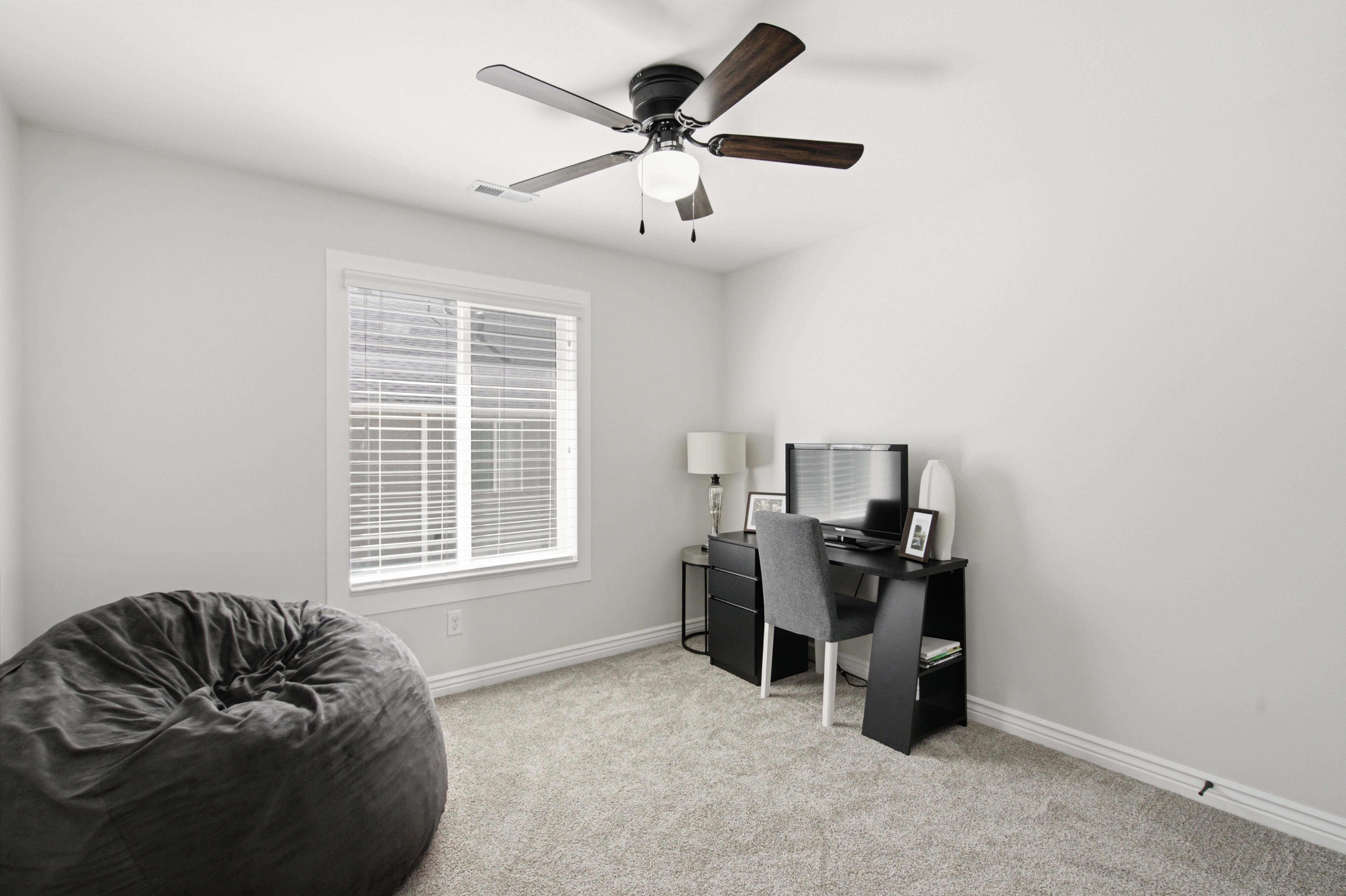Bright interior room featuring a window with blinds, a ceiling fan with light fixture, light gray carpet, white walls, and white baseboards
