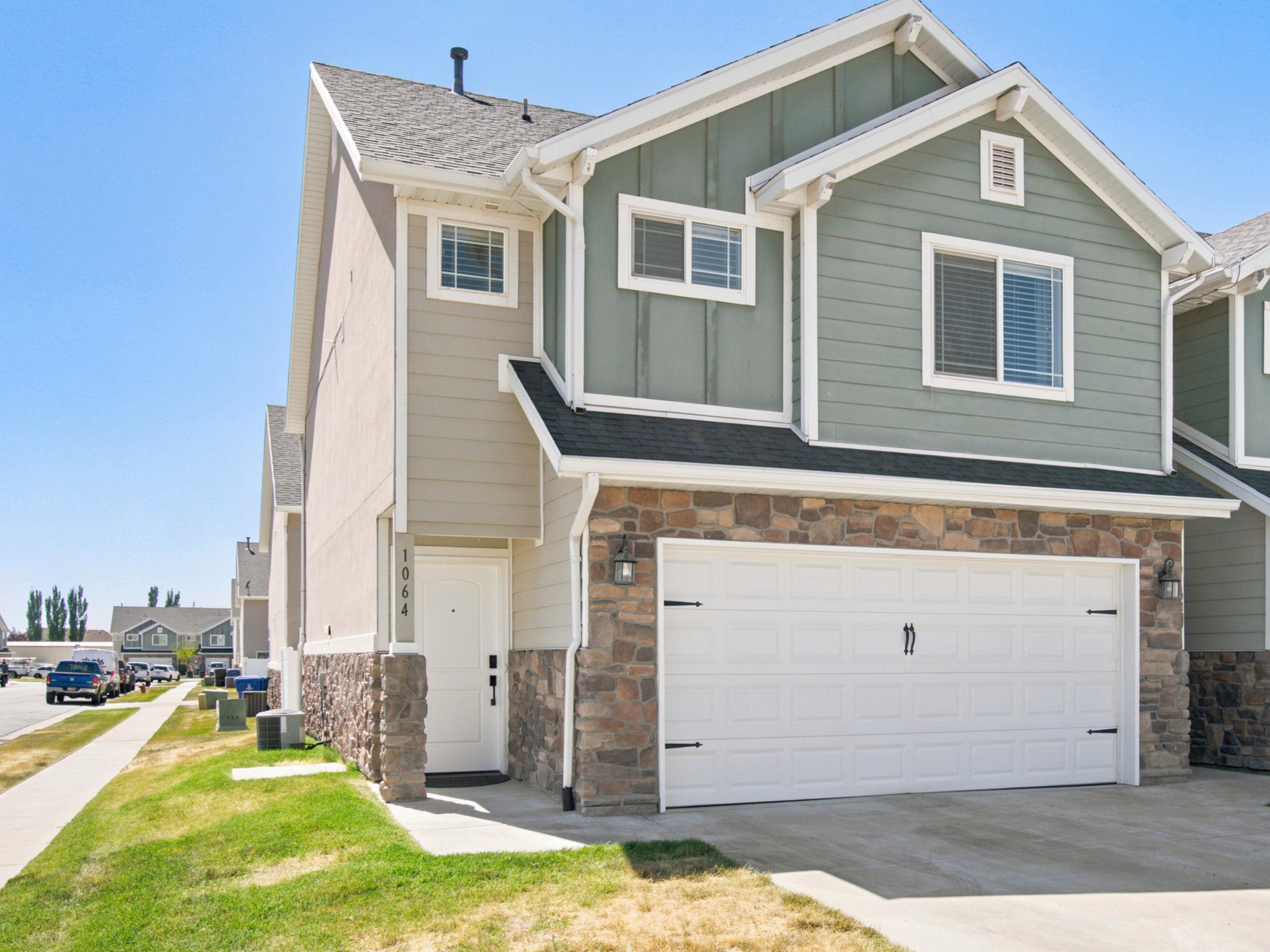 Modern townhome-style residence featuring a two-tone facade, stone accents, attached garage, concrete driveway, and a white entry door