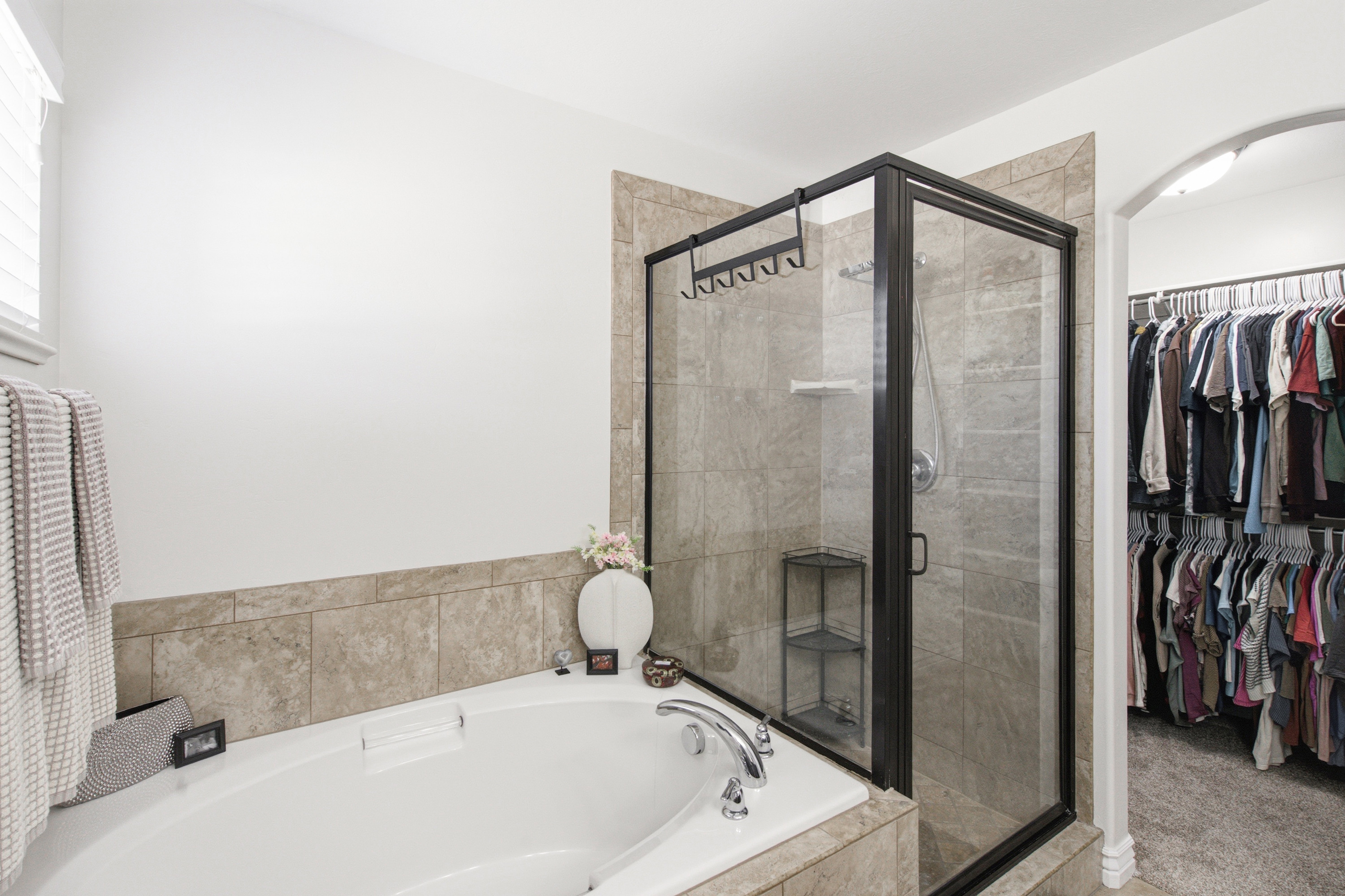 Bathroom featuring a built-in soaking tub with tiled surround, a glass-enclosed shower with tile walls, and an arched entry to a walk-in closet with extensive hanging storage